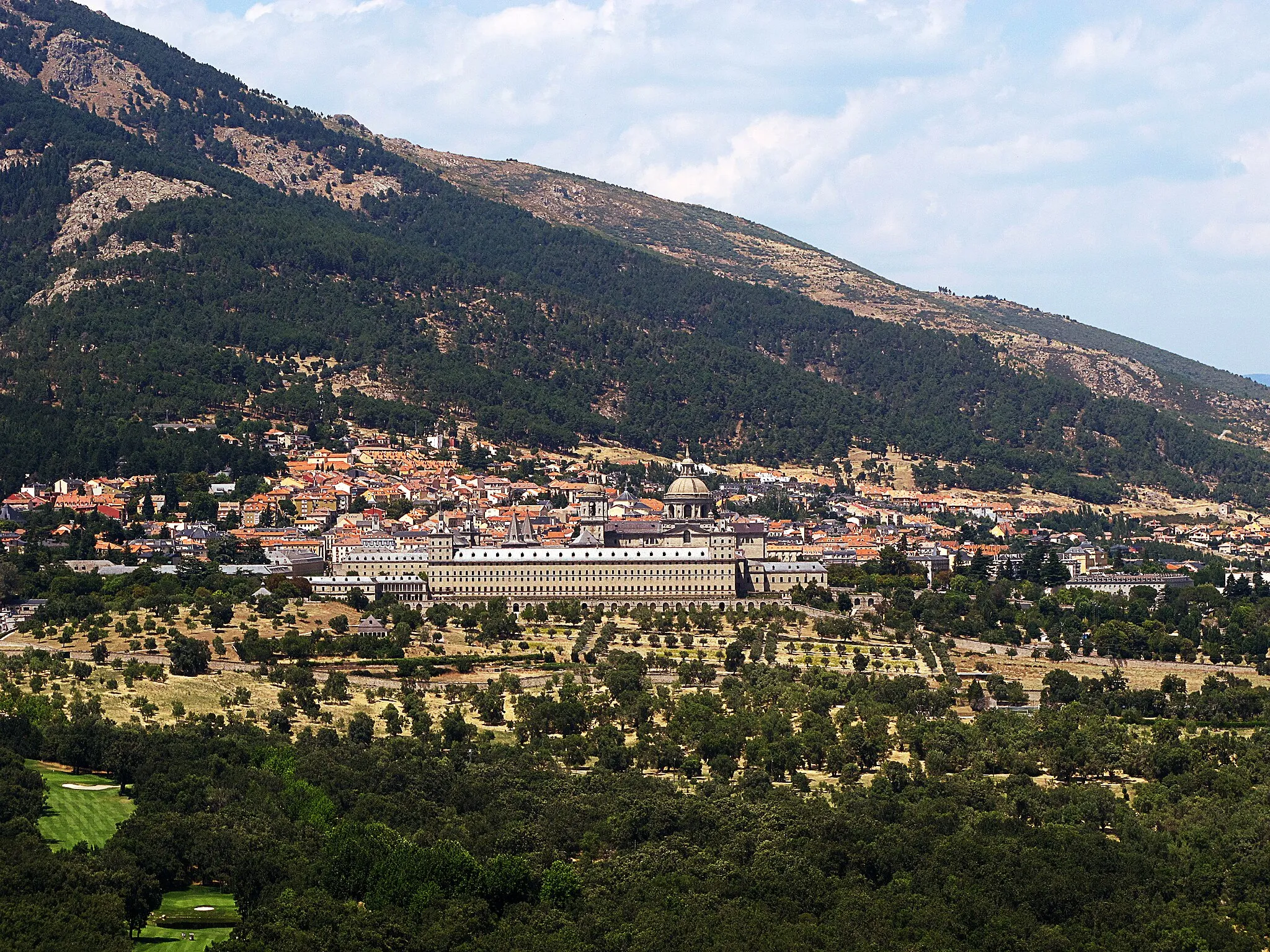 Photo showing: El Monasterio de El Escorial
Como los templos cristianos, el monasterio está orientado siguiendo el eje Este-Oeste, aunque con una peculiaridad: está ligeramente desviado, de tal forma que su fachada Oeste se alinea a la perfección con la puesta de sol del día 10 de agosto, fecha de la victoria de San Quintín y festividad de San Lorenzo.
Cumplió las funciones de monasterio, palacio, museo, biblioteca etc., fue erigido por el monarca para conmemorar la victoria de la batalla de San Quintín frente a las tropas francesas. Pero, al mismo tiempo –y según algunos autores– posee una segunda lectura de corte hermético.
Una tradición muy arraigada en la época afirmaba que en El Escorial estaba la boca del infierno. Existen leyendas que atribuyen al Diablo un papel estelar en ese enclave y se ha llegado a decir que Felipe II pretendió tapar esa entrada al inframundo colocando encima el monasterio.
Curiosamente, la basílica del templo alberga un cuadro de Sánchez Coello donde aparecen San Jerónimo y San Agustín y en el que éste último porta una maqueta del edificio mientras un niño señala un agujero en el suelo. ¿La boca del infierno?

Dado el carácter esotérico que está presente en el edificio ¿está realmente el Monasterio sellando la entrada del infierno o por el contrario sería una puerta de acceso al inframundo…?