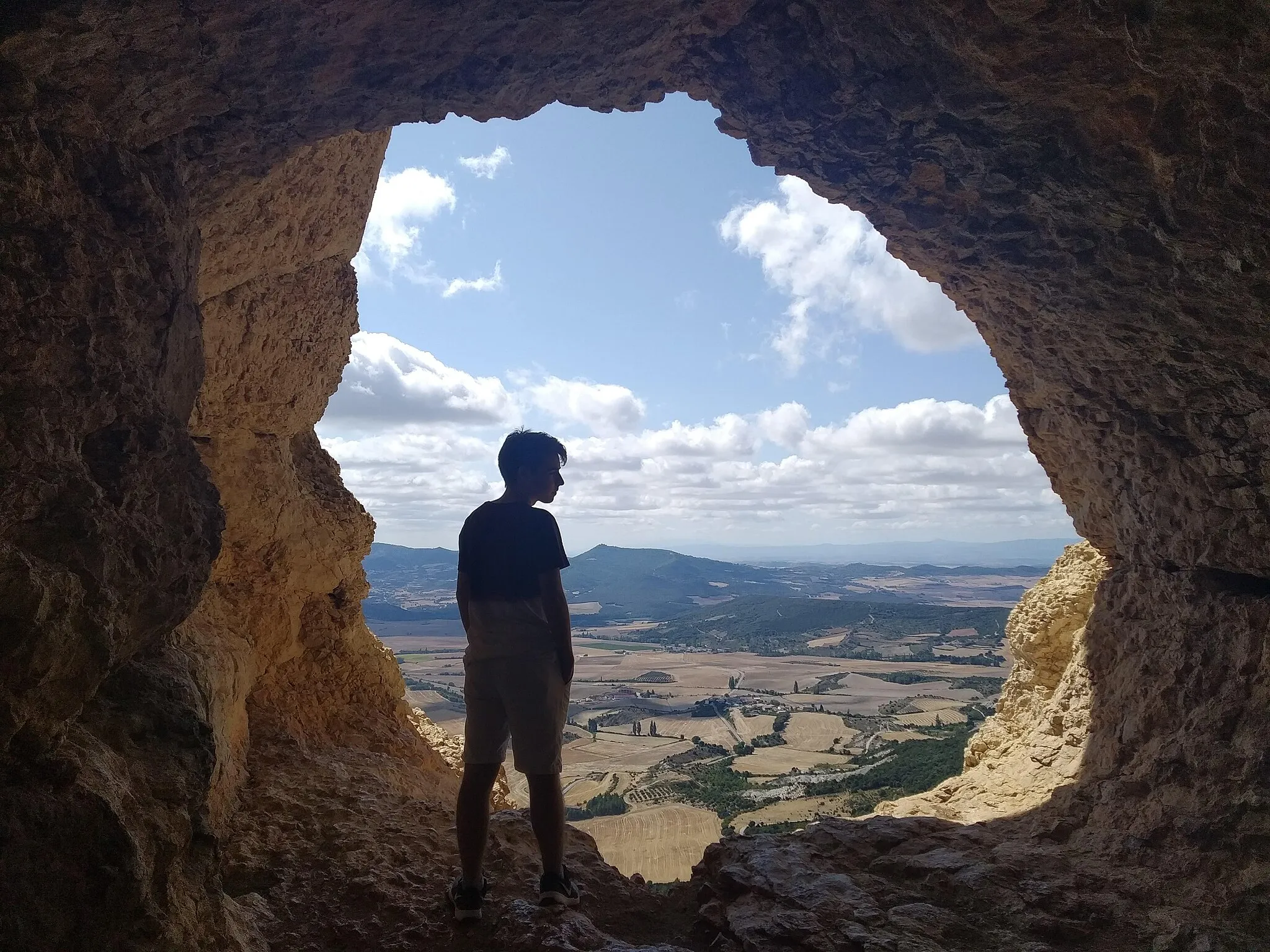 Photo showing: Vista del Ojo de San Prudencio desde el interior de la cueva, con la silueta de un joven recortándose ante el paisaje del valle de Allín