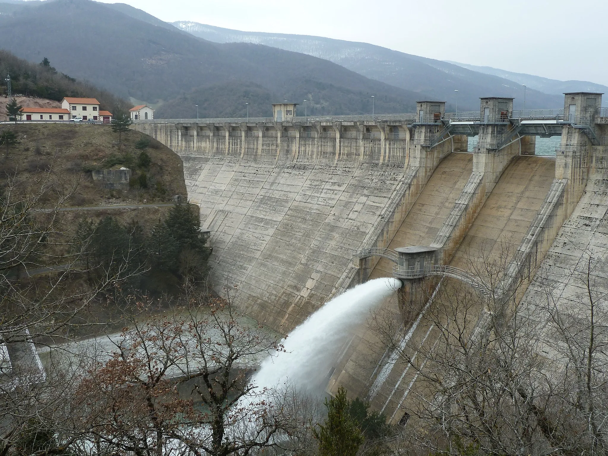 Photo showing: The dam of Eugi, in operation since 1973, is located in the valley of Esteribar (26 kilometers from Pamplona). Its construction began in 1966 to ensure supply to the growing population and industry of Pamplona and its area, which previously was supplied by the spring of Arteta, in use since 1886, because this spring was no longer able to meet the demand for water, especially in times of drought. It is a gravity dam ground curve and its height above the level of the river is 44.3 m.