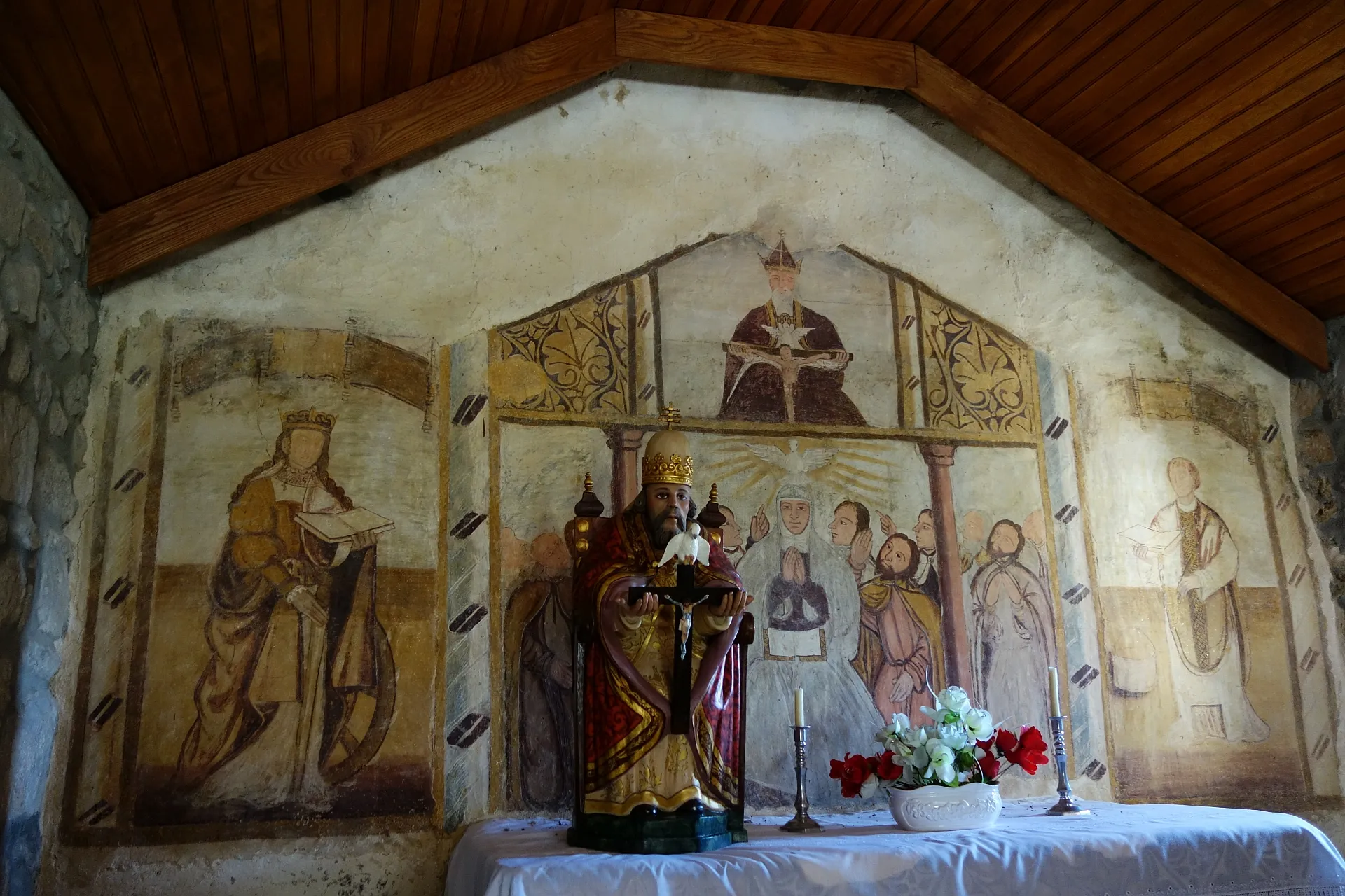 Photo showing: Mid-16th century mural painting in the Chapel of the Holy Spirit, Maçaínhas, Belmonte. There is no documentation about the authorship of the paintings, the date and their meaning, although several art historians have looked into it since their discovery in the 1980's. The panel on the left is thought to represent Saint Catherine, due to the characteristic combination of symbols: the wheel, the sword and the book. The panel on the right represents an unidentified male figure, thought to be a saint, for symmetry with Saint Catherine. The bottom of the middle panel represents the event of the Pentecost, i.e. the Holy Spirit's descent onto the apostles, with the Holy Virgin at the center of the picture. The top of the middle panel represents the Holy Trinity. (See repositorio.ucp.pt/bitstream/10400.14/4455/4/LS_S2_13-14_...)

The statue of the Holy Trinity that has been placed in front of the mural is more recent.