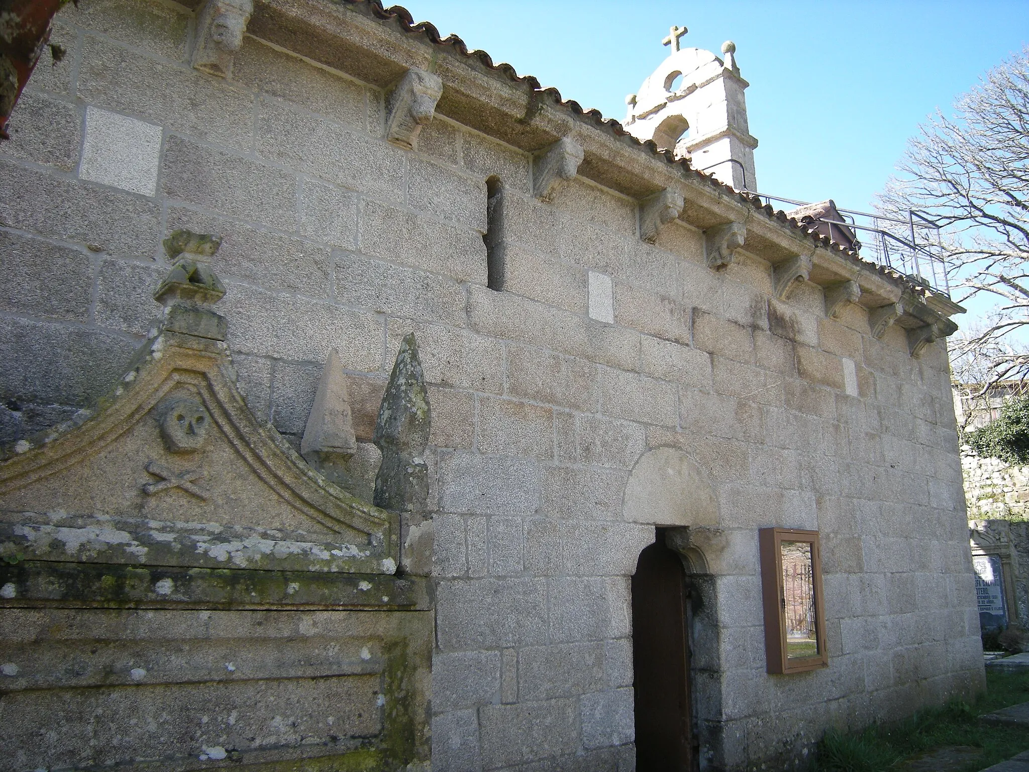 Photo showing: En el muro norte de la nave, se abre una saetera y una sencilla portada con dintel liso apoyado sobre ménsulas.

En la cornisa, varios canecillos completan la decoración.