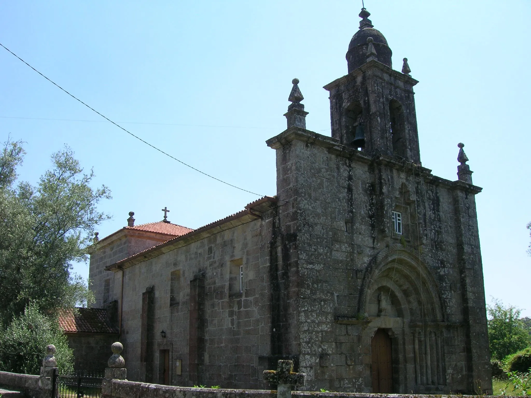 Photo showing: Vista noroeste de la iglesia en la que vemos la amplia portada románica.

En los muros norte y sur del ábside conserva dos ventanas saeteras tapiadas.
