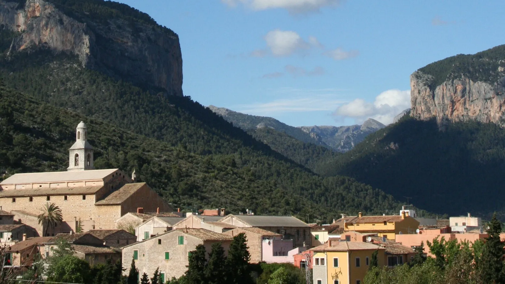 Photo showing: A view over the village to the mountains taken from the road that runs alongside the village school.
The mountains are: Puig d’Alaró (left) and Puig d’Alcadena (right)