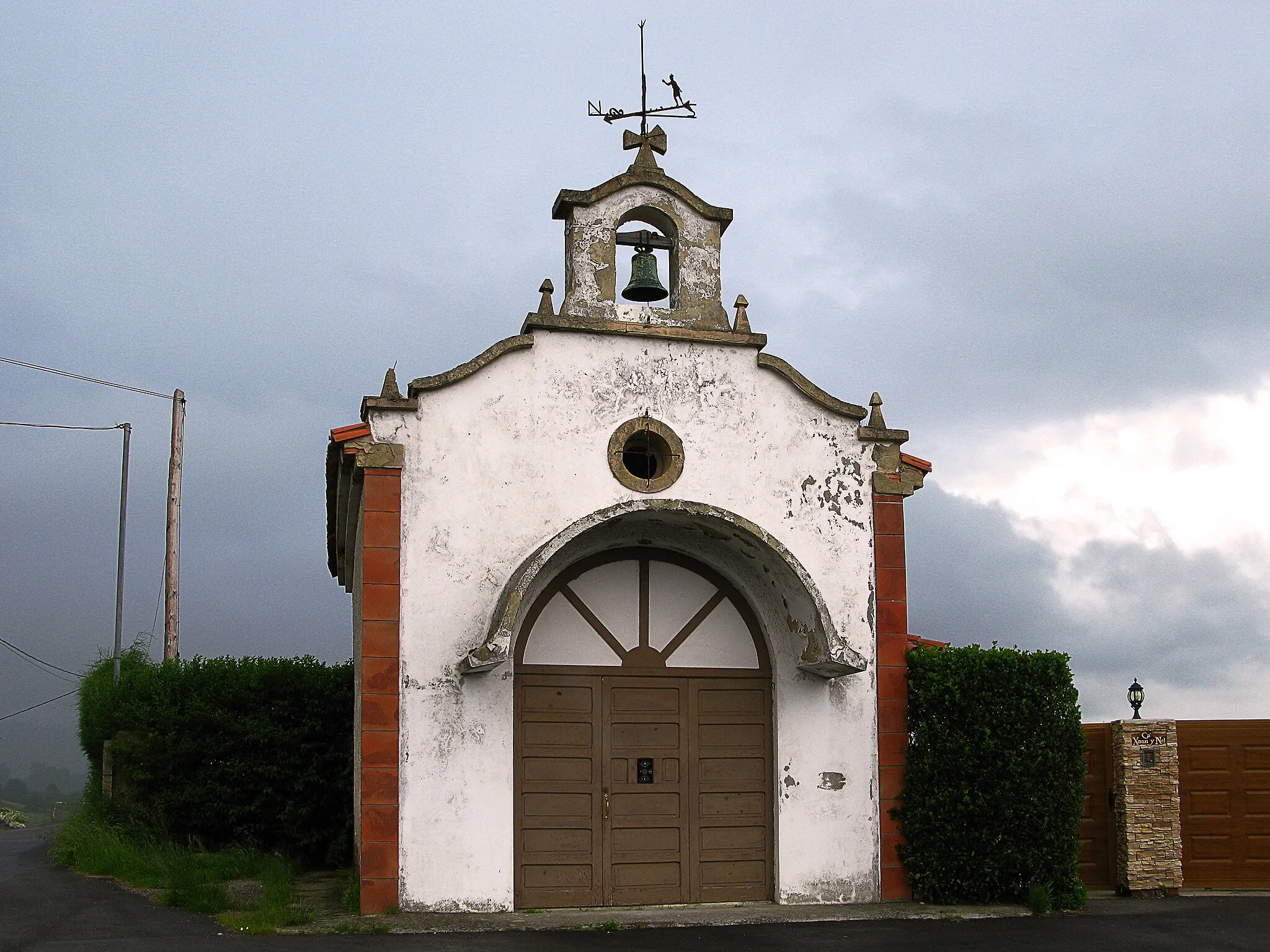 Photo showing: Se trata de adivinar el lugar de la fotografia.....
De esa capilla llama la atencion el ornamento de su veleta, 
Muchas veces es solo una pieza metálica giratoria, con forma de flecha, que sirve para señalar la dirección del viento.
Otras es  la figura de un gallo usual en  cimborrios de la catedrales y de las torres de las iglesias y se justifica por el poder que se le atribuía a esta ave de ahuyentar al demonio, entre otros poderes y supertisticiones
Parece que la veleta ya aparecía como signo cristiano sobre iglesias y monasterios en el siglo IX,  entre los que el gallo era el simbolo  de los más utilizados
Tambien se advierte en las veletas  que el diseño del elemento decorativo  que se elige, casi siempre es  un símbolo, estatus, aficion o pasatiempo , por lo que  a menudo define al  propietario

Santa Apolonia es una mártir que murió en Alejandría (Egipto) a mediados del siglo iii, a durante un levantamiento local contra los cristianos. 
En ese tiempo Apolonia, parthénos presbytis, era considerada importante. Estos hombres la agarraron también y con repetidos golpes rompieron todos sus dientes. Entonces amontonaron palos y encendieron una hoguera afuera de las puertas de la ciudad, amenazando con quemarla viva si ella se negaba a repetir, después de ellos, palabras impías, como blasfemias contra Cristo o invocación a dioses paganos. Por petición propia, fue entonces ligeramente liberada, saltando rápidamente en el fuego, quemándose hasta la muerte.
Está considerada la patrona de la odontología y los Cirujanos Dentistas
En la Edad Media solía decirse que cuando se tuviera un dolor de muelas se rezaba a Santa Apolonia y el dolor desaparecía.
Santa Apolonia es la patrona del lugar, que tiene aquí una capilla a ella dedicada.
Tal y como esta documenta,  la capilla  fue construida en 1954,  e inaugurada en el mes de agosto, coincidiendo con las fiestas del pueblo 
Seis décadas después en el año 2014, se entraba en la capilla para realizar una intervención que  clamaba desde hacía varios años.

Además, se recuperó la veleta,  una figura humana que avanza hacia una hoguera, en alusión al martirio de Santa Apolonia.