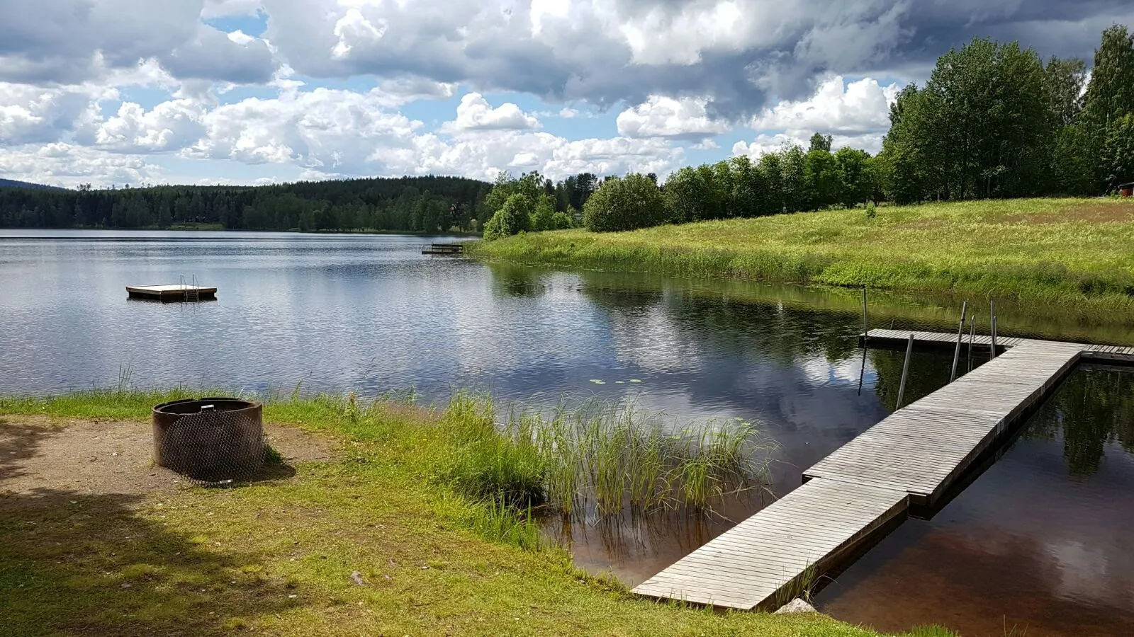 Photo showing: Bilden visar del av Skidtjärnnen sett från Lillviksbadet i sydvästlig riktning. I förgrunden till vänster grillplats och till höger en del av badbryggan. Längre ut ligger en flytbrygga där badande kan vistas på.