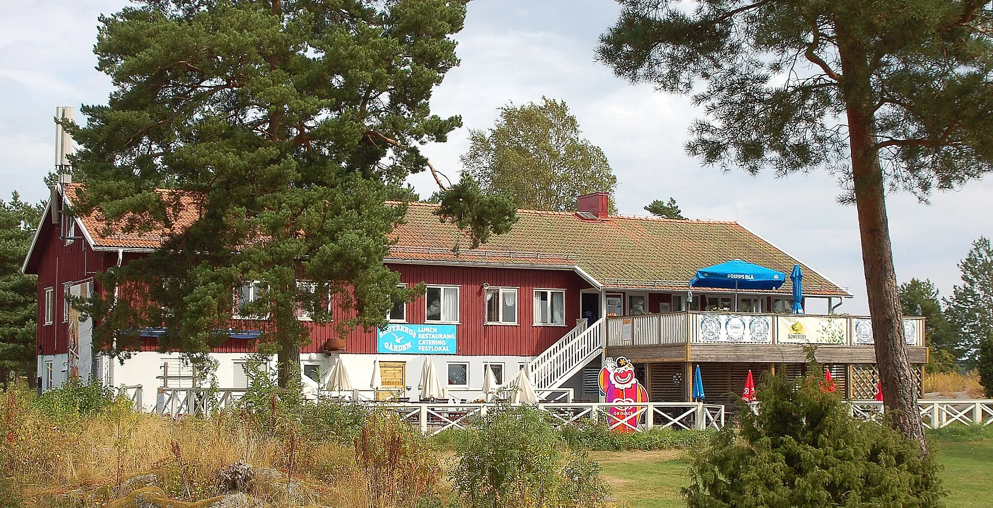 Photo showing: Skutbergs gården. Skutbergsgården speglar inte bara Skutbergets utveckling från jordbruk tillhörande gården Eriksberg till friluftsområde, utan är även ett belysande exempel på friluftsrörelsens framväxt i Sverige. Den traditionella allmogestugan med rödfärgad panel, vita snickerier och lertegel står som förlaga för arkitekturen. Bortsett från den utbyggda balkongen och staketet har byggnaden i stort bibehållit sitt ursprungliga uttryck. Byggår 1955, Arkitekter var Olle Lagergren och Nils Åkerman. Byggnad i två våningar där det första planet utgörs av en vitmålad sockelvåning. Fasaden är täckt av stående rödmålad locklistpanel med vita snickerier kring tvåluftsfönstren och dörrarna. De vitmålade trädörrarna har i den övre delen ett glasparti. Mot söder har balkongen byggts ut och ett vitmålat staket tillkommit. Vid norra fasaden finns en vitmålad trätrappa upp till andra våningen. Sadeltaket täcks av tvåkupigt lertegel och kröns av ett flertal skorstenar. Utbyggnad av balkongen 2008 och ett senare tillkommet staket. Flera utbytta dörrar. Ursprungligen invigdes Skutbergsgården 1955 som samlingslokal för friluftsidkare på Skutberget. Uppförandet initierades av Friluftsfrämjandet. Idag används lokalerna som restaurang med catering och uthyrning av festvåning