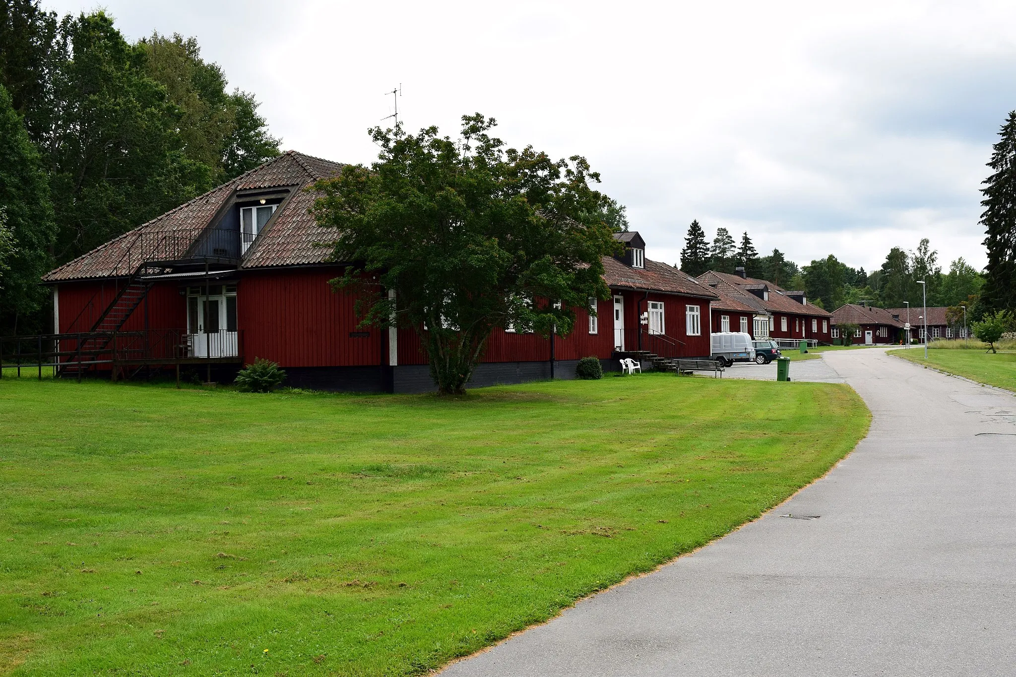 Photo showing: Byggnaderna uppfördes ursprungligen som kaserner till Göta trängregementes kompani i Nora. Kasernerna är uppförda som plutonskaserner i ett plan med källarvåning. Varje kasern bestod av åtta logement med en genomgående korridor och hade förläggningsutrymme för 48 personer plus fyra furier fördelade på två underbefälsrum. Kasernbyggnad 3 kallades för Främlingslegionen, det på grund av att den inhyste värnpliktiga som inte kom från ett trängförband. Bilden föreställer kasernerna med matsalsbyggnaden längst bort.