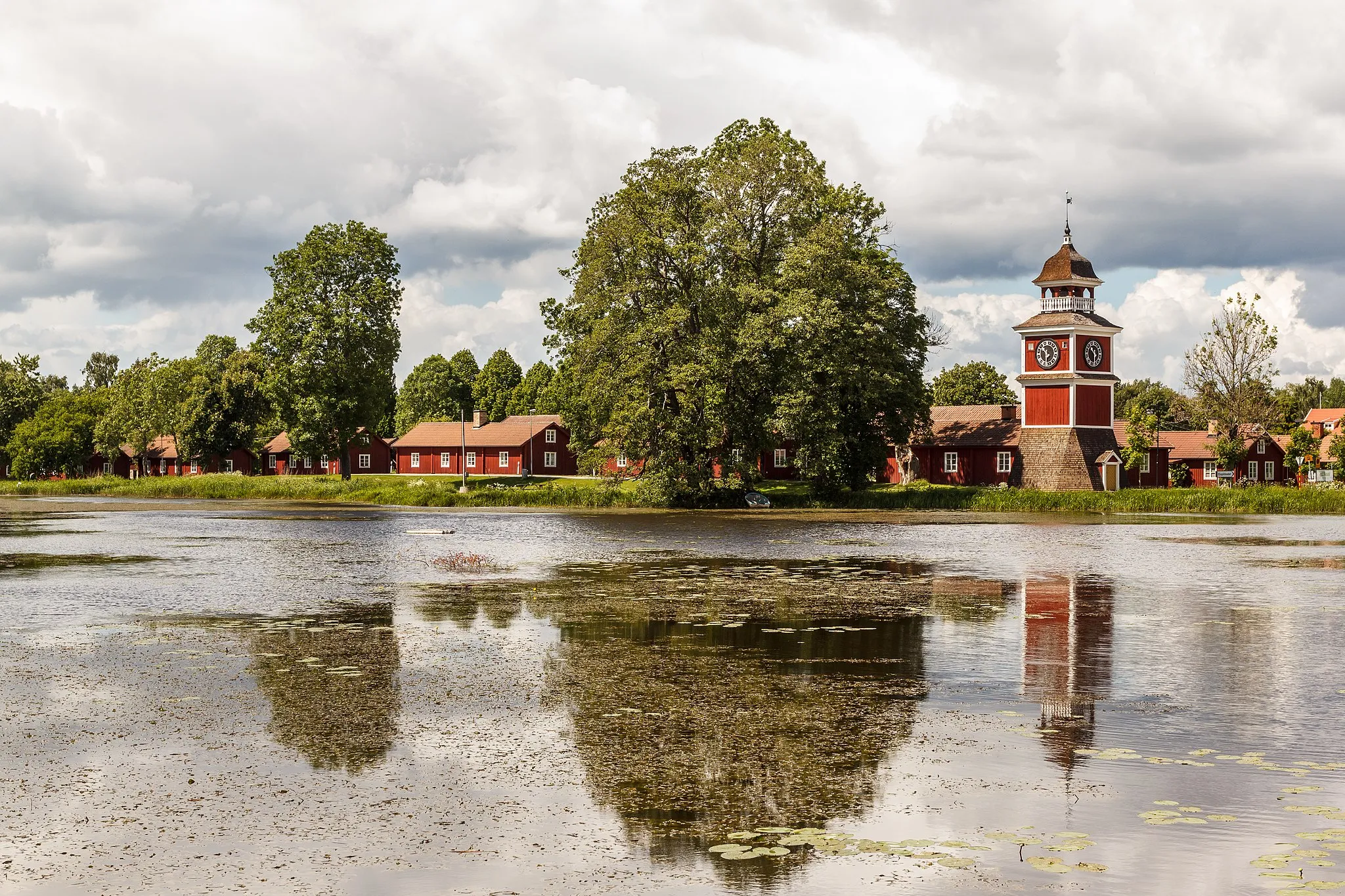 Photo showing: Dam in stream Tämnarån ("[Lake] Tämnaren stream") at Karlholm former ironworks, Karlholmsbruk, Sweden. Workers housing and belfry in background.