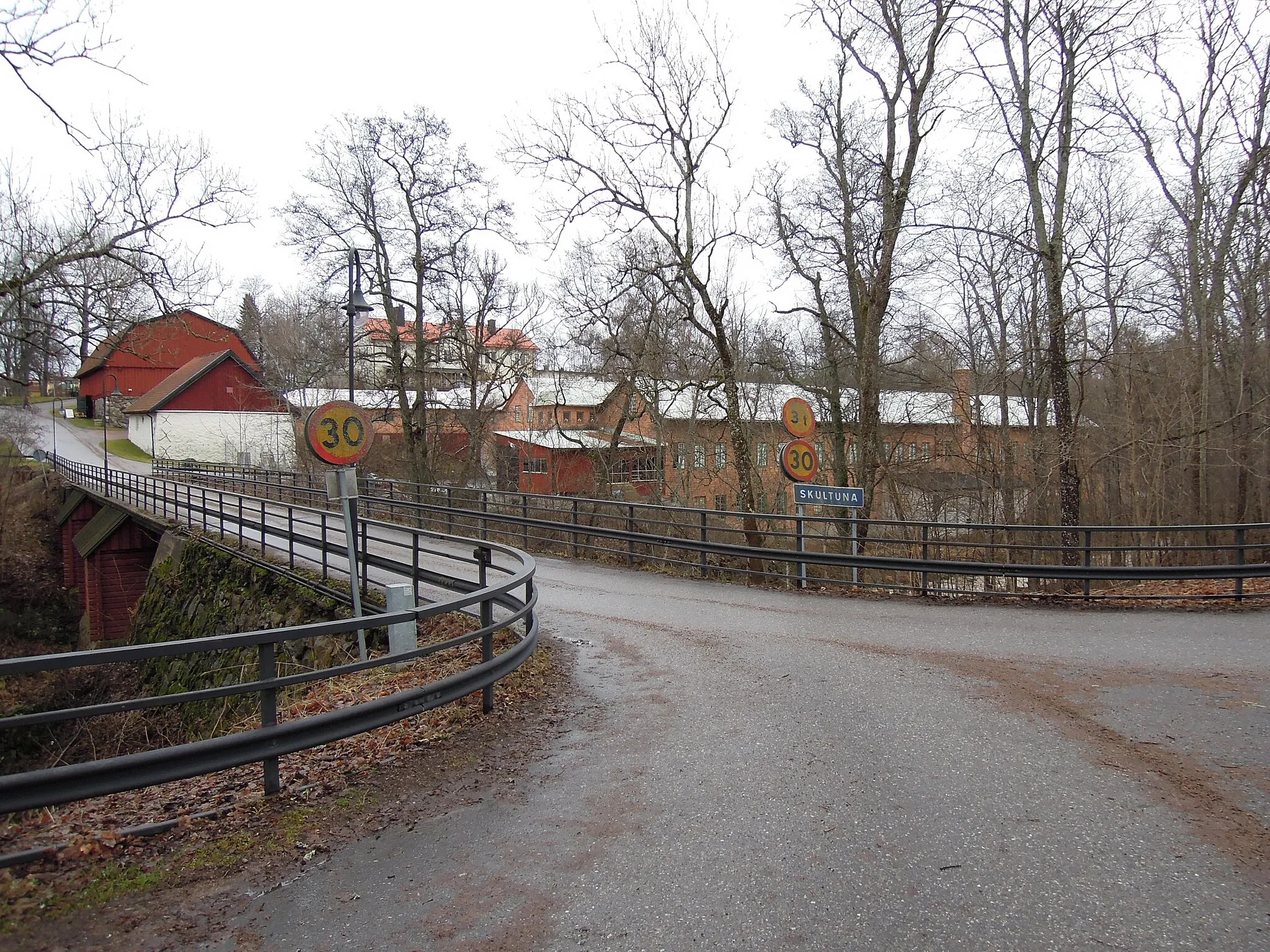 Photo showing: Skultuna Messingsbruk (Brass manufacturing industry) outside Västerås, Sweden. The entry road over the brook, from left: coal barn, hotel, manufacturing plants.