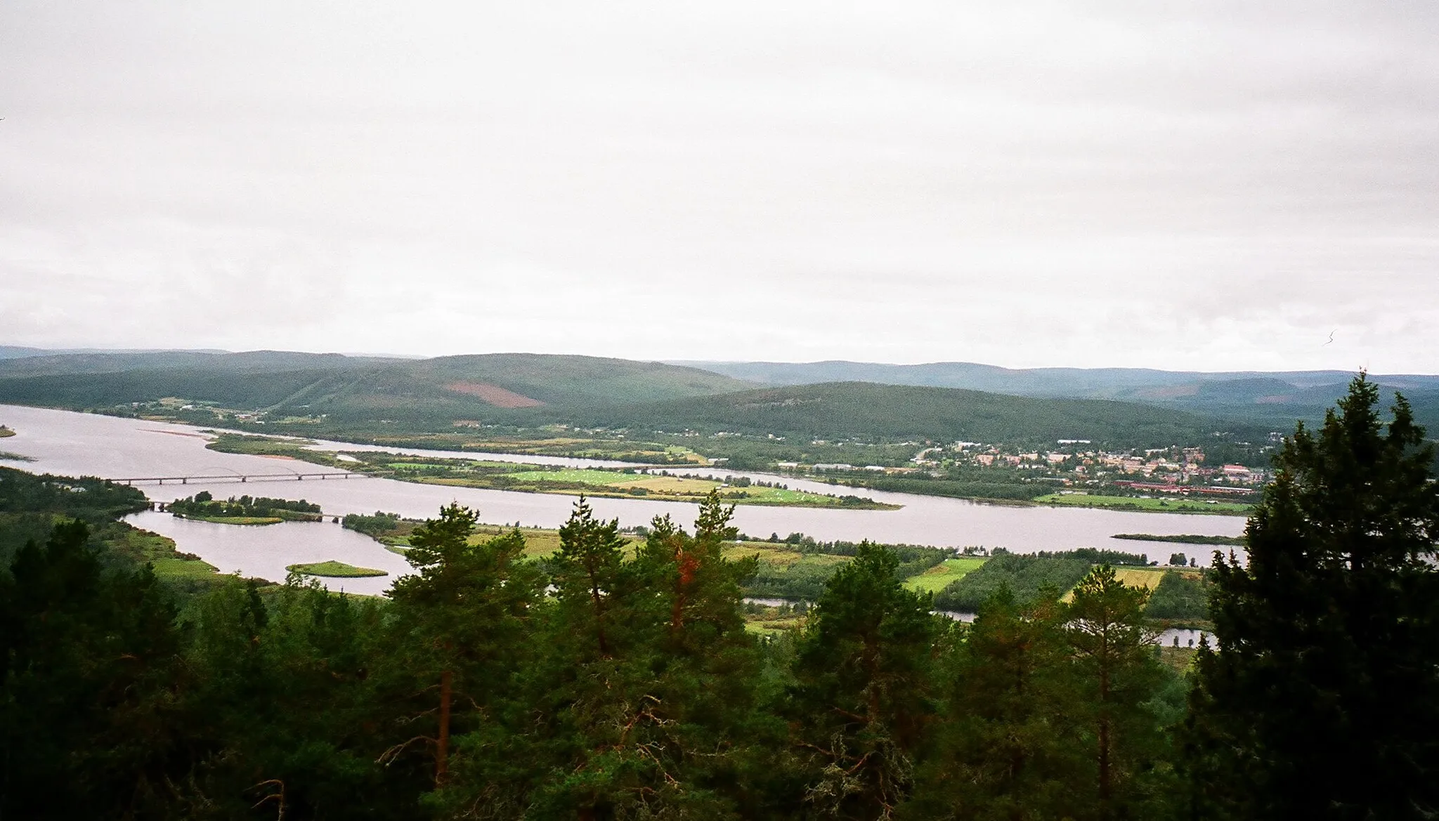Photo showing: View to the west from the observation tower atop Aavasaksa hill in finnish Lapland. The wide Tornio river is flowing towards the left of the picture. The big village visible is Övertorneå-Matarengi in Sweden. On the far left the bridge marks one of the border points between Sweden and Finland.