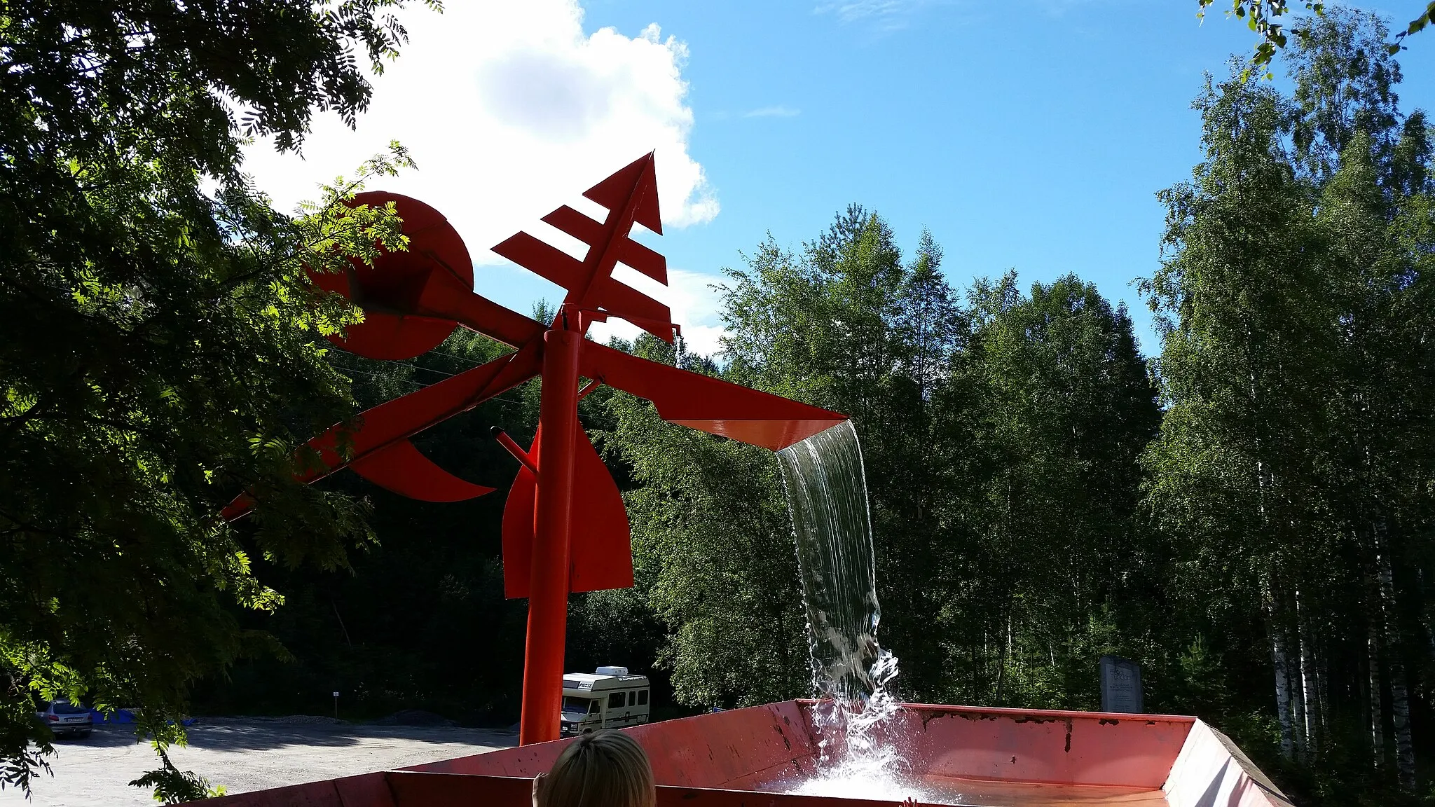 Photo showing: Konstverk av Ante Dahlstedt som står på den gamla flottningsrännan. Den symboliserar flottningen i Umeälven med symboler för skogen, flottarens hatt, båtshaken och åran. Konstverkets ena horisontella arm fylls långsamt på med vatten tills dess att konstverket tippar några grader åt sidan och släpper vattnet ner i den gamla flottrännan.