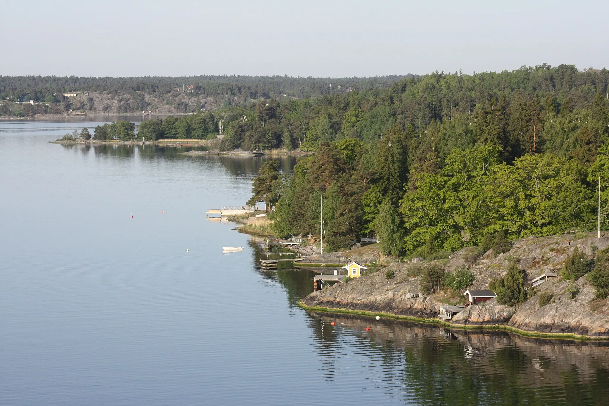 Photo showing: The south-eastern shore of Skogsön island in the Stockholm archipelago. Skogsö Södra jetty, served by Waxholmsbolaget ferries, can be seen on the nearest part of the island (with the yellow shelter). Beyond Skogsön can be seen the southern tip of Tynningö island, and the Norra Lagnö shore of Varmdö island.