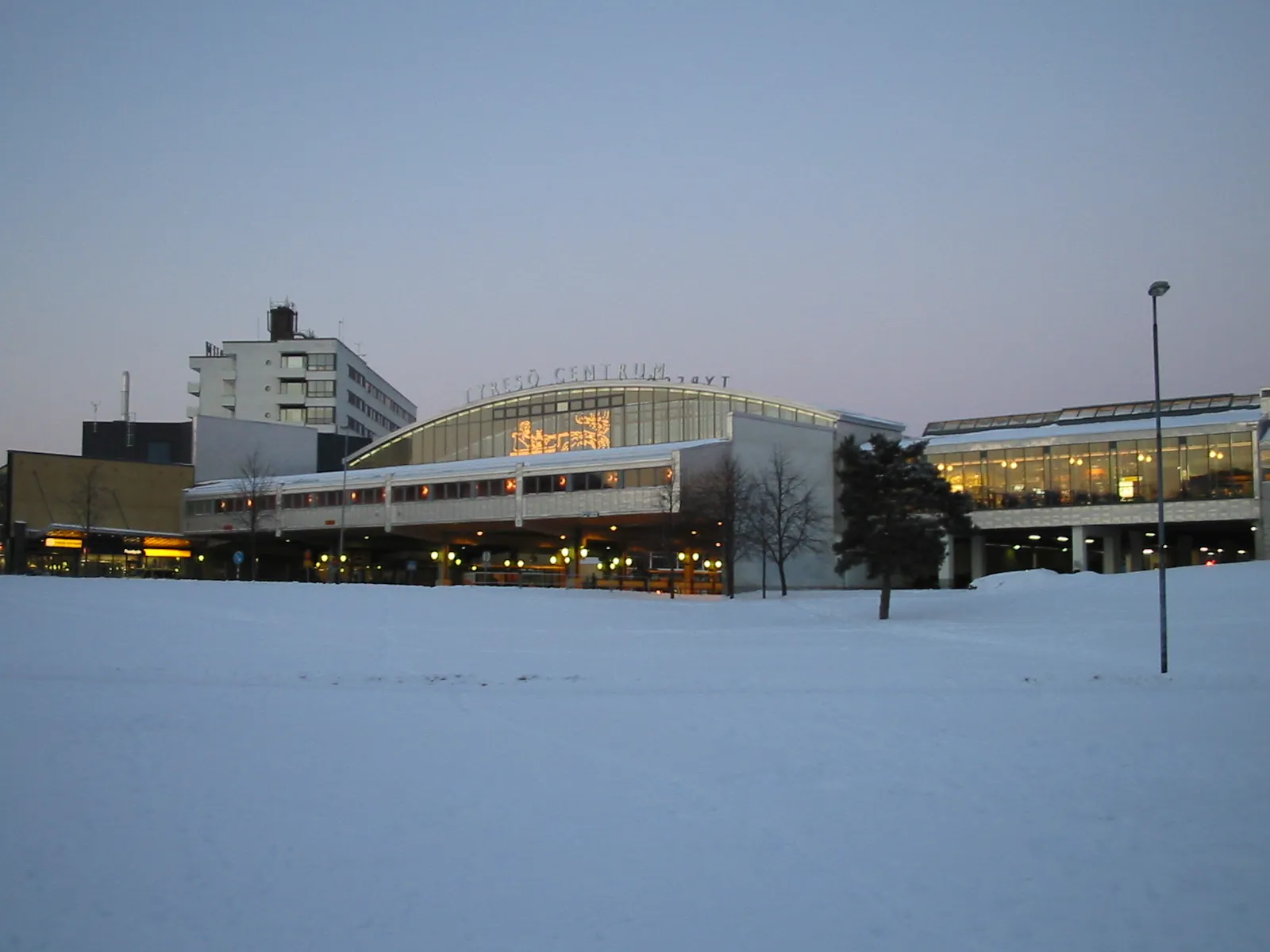 Photo showing: *The Tyresö Centrum enclosed shopping centre, in Tyresö centre, Bollmora, Tyresö Municipality, Sweden, during winter. Image taken from south.
The municipal hall of Tyresö is the tall building on the left. It is completely enclosed by the shopping centre
The Tyresö centre bus terminal is beneath the bridgelike structure of the shopping centre.