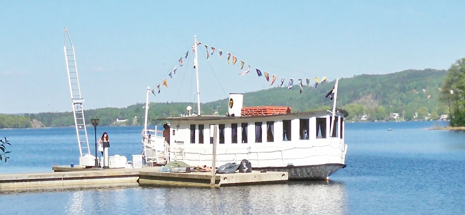 Photo showing: M/S Svanen (The Swan) moored to its quay in the southside Almenäs cove of the lake Öresjö. It has a restaurant on board and sometimes live musical entertainment during its sightseeing routes around the lake.