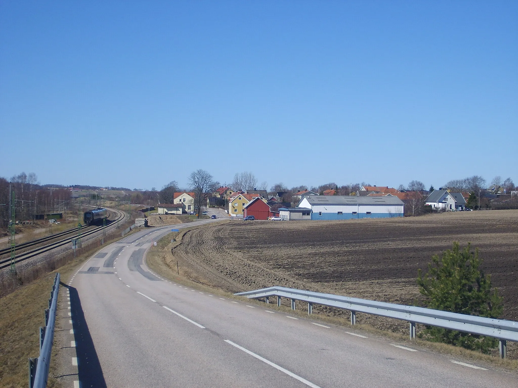 Photo showing: View of Heberg, a community in Sweden. West Coast Line (Västkustbanan) with an Oresundtrain (Öresundståg) is shown at the left. The white building between the tracks and the road used to be a train station in the past.