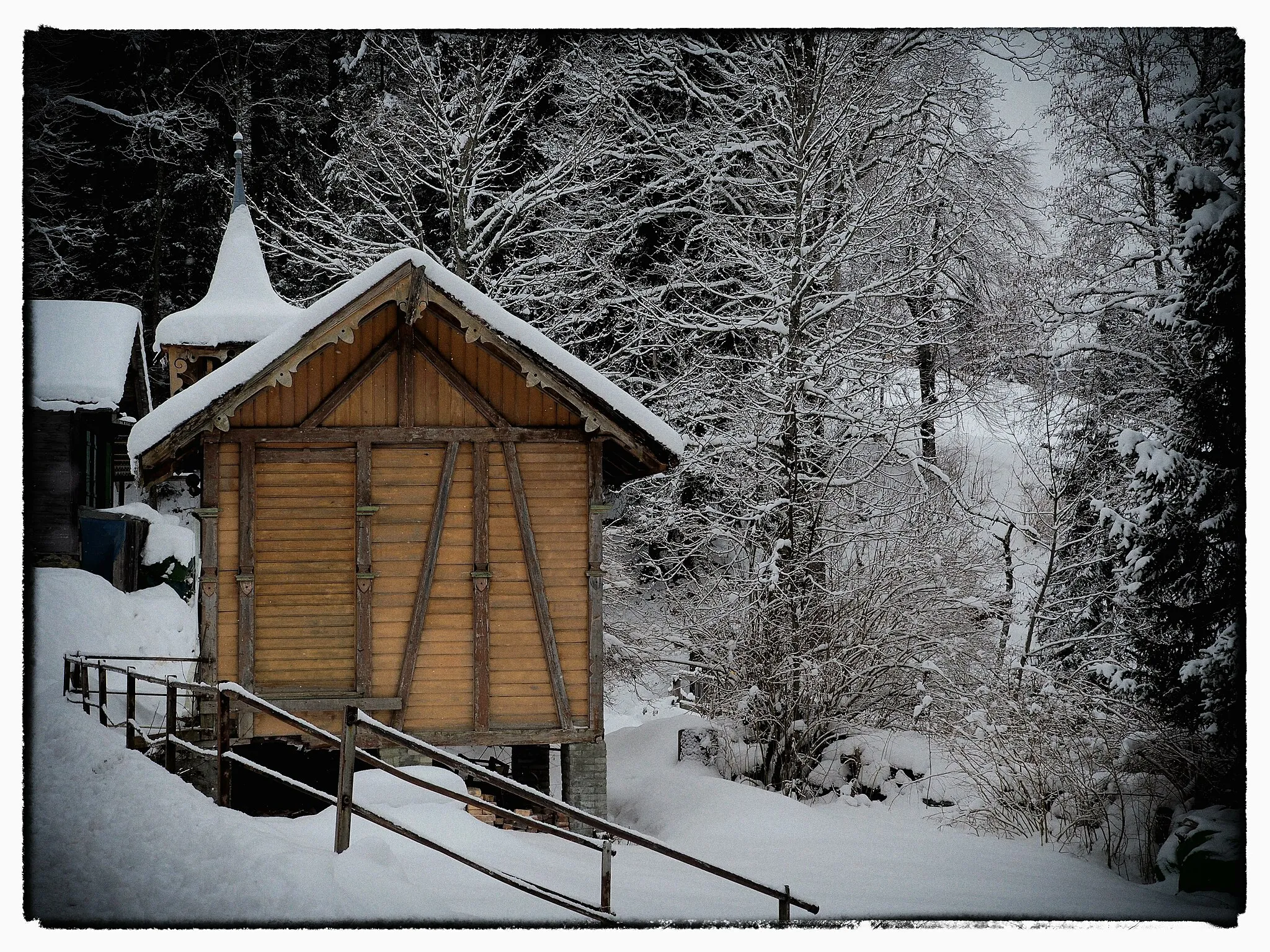 Photo showing: This Chapel is on the road from Wengen to Lauberhorn chair lift. It's in a bit of a state awaiting refurbishment - a sign says all money gratefully received. There was a very restricted angle to get the shot without capturing plastic, rope and tarps used to seal it up.

Post processed using Google's now free Color Efex Pro, with Vintage Recipe which is hiding a few modern tarps in the edges of the shot. I took the liberty of Photoshopping out the Recycling sign on the far left building.