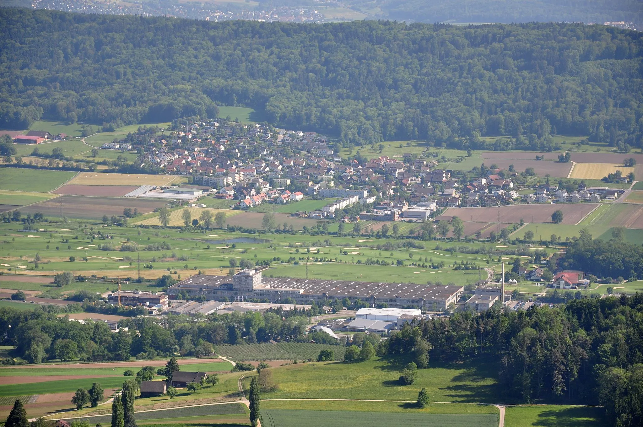 Photo showing: Dänikon on the northern slope of the Altberg in the back with the eastern end of Otelfingen's industrial area in the foreground and part of the Golfpark Otelfingen in between as seen from Burghorn respectively Jura-Höhenweg on Lägern (Switzerland)