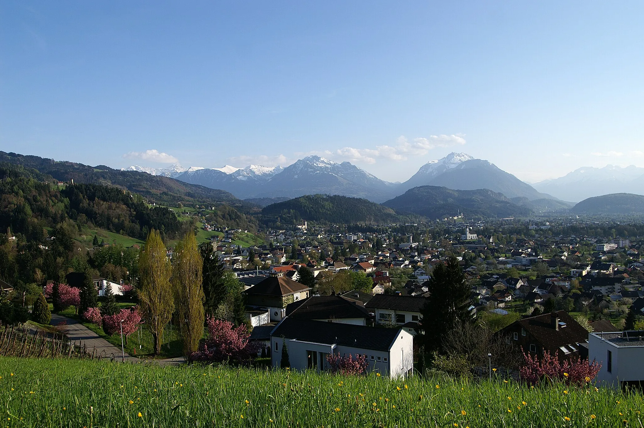 Photo showing: Blick von der Rebhalde, oberhalb von Röthis über die Kirchtürme von Zwischenwasser, Sulz, Rankweil auf die Berge des noch verschneiten Rätikon in Vorarlberg. Die Kirschblüte hat begonnen.