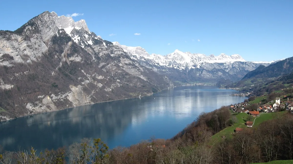 Photo showing: Walensee as seen from Kerenzerberg towards East. Kerenzerberg was the ancient road for the steep shore of the lake, there's no road to the settlement Quinten on the northern shore. Mountains are Churfirsten the row to the left and Sichelchamm the distinct triangle at the far end.
