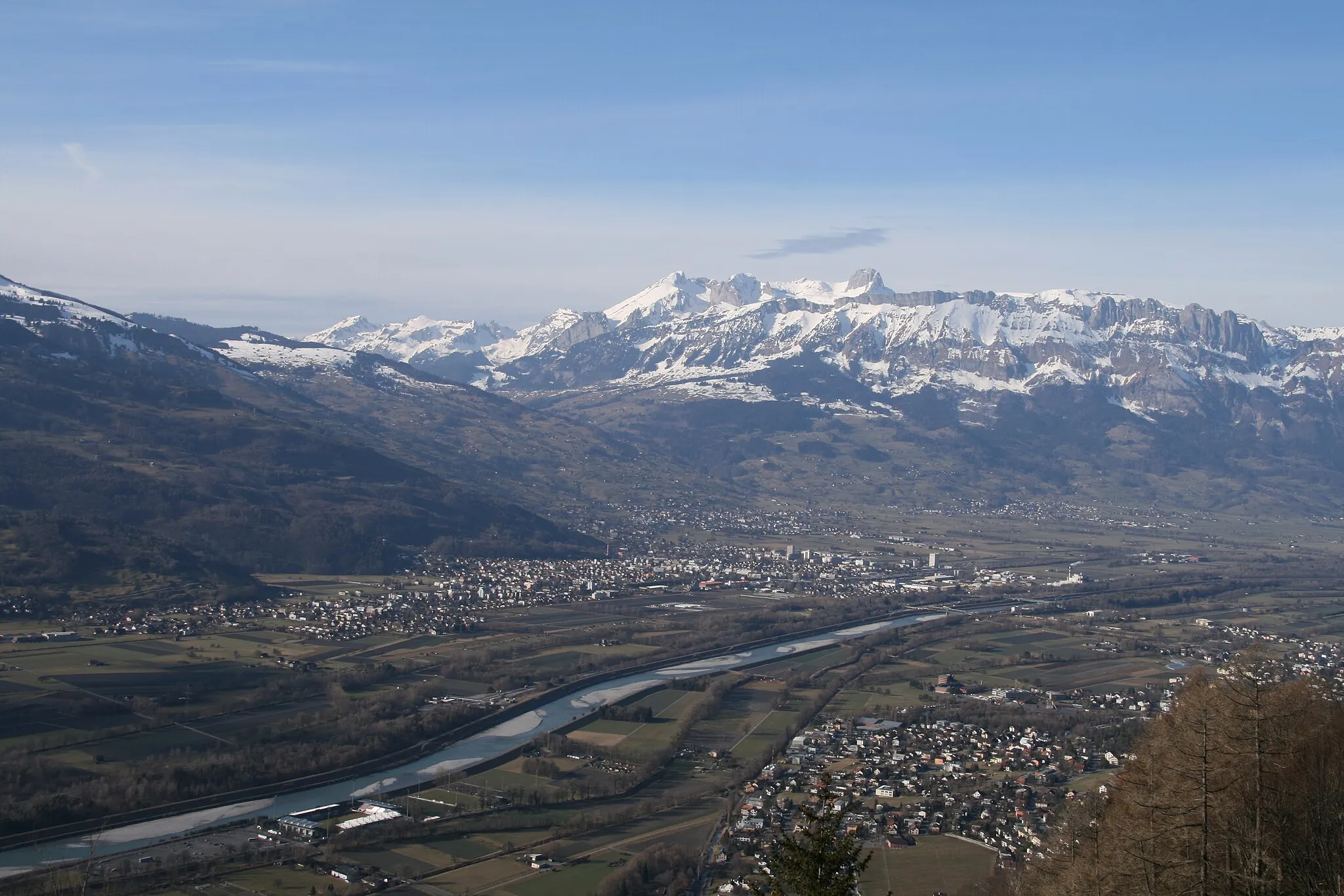 Photo showing: Blick von Triesenberg talwärts auf rechts die Gemeinde Schaan in Liechtenstein über den Alpenrhein hinüber auf die Gemeinden Buchs SG, Grabs und Gams SG auf die noch schneebedeckten Berge des Alpsteines.