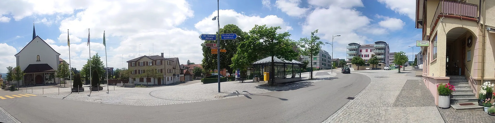 Photo showing: Panoramaansicht des Dorfzentrums von Engelburg mit Kirche, Friedhof, Postautohaltestelle, E-Auto-Ladestation und der Hauptstrasse, die links St. Gallerstrasse und rechts Tannenbergstrasse heisst.