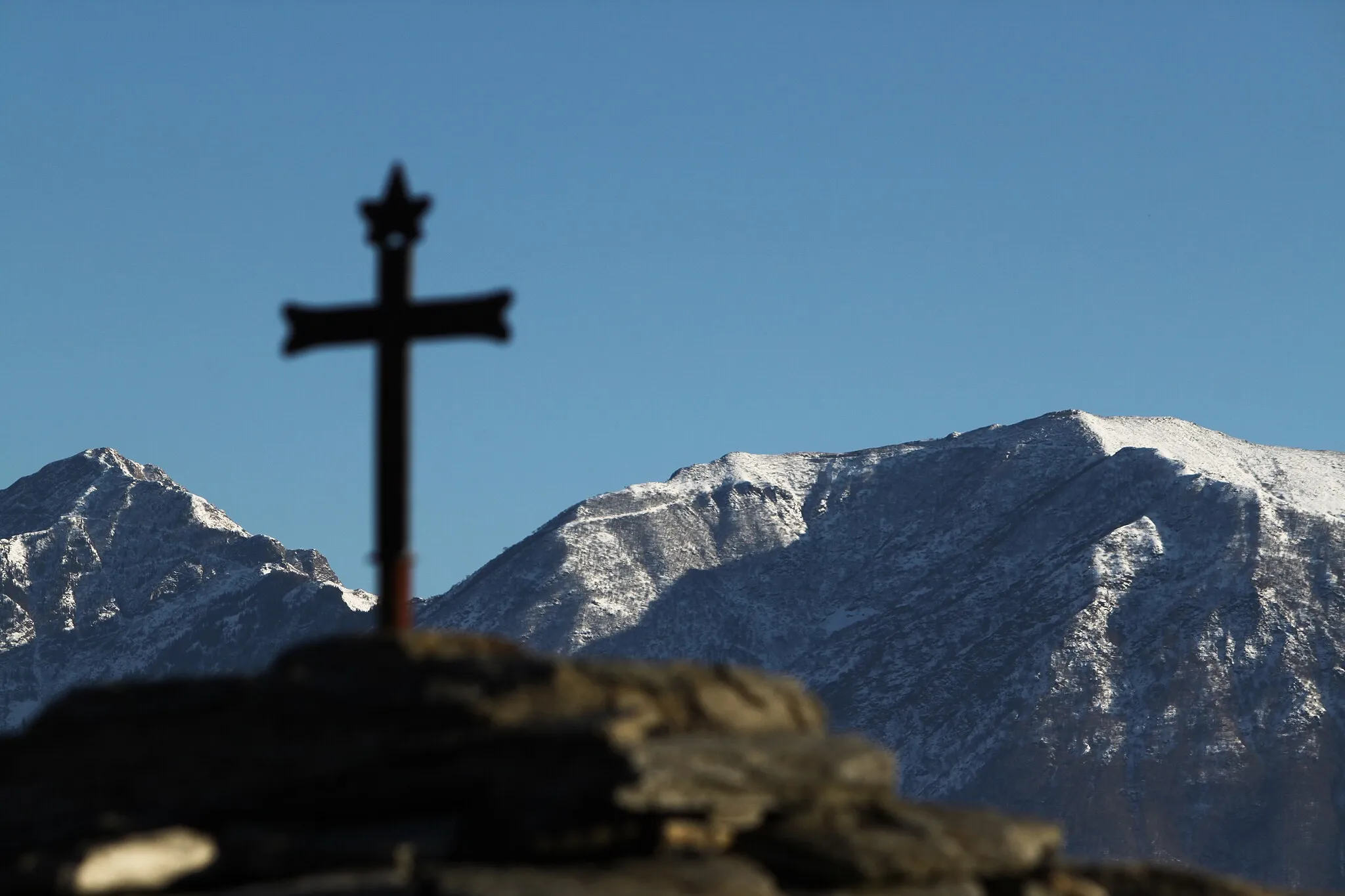 Photo showing: Cross over the slate roof of a chapel at Comoi, Tegna. In the background the Lugano Prealps.