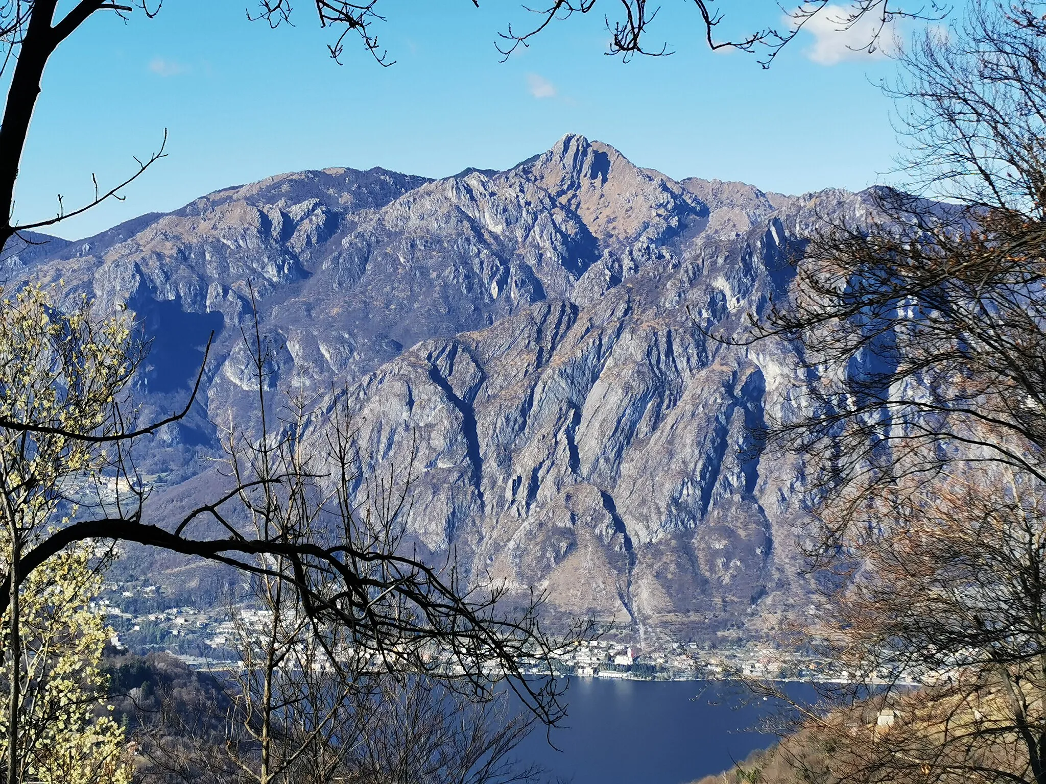 Photo showing: Panorama in direzione nord sul lago di Lugano, ripreso da un'area pic-nic lungo la Strada del Ross, nel comune di Laino. Al centro della foto, la vetta più alta è la Cima di Fiorina (o Cima di Fojorina, come la chiamano gli svizzeri), lungo il confine italo-svizzero. A sinistra della Cima di Fojorina, su un piano più vicino, il Monte Pradè. A destra della Cima di Fojorina, in primo piano, la cima ovest del Monte dei Pizzoni (quella est è coperta dai rami degli alberi).