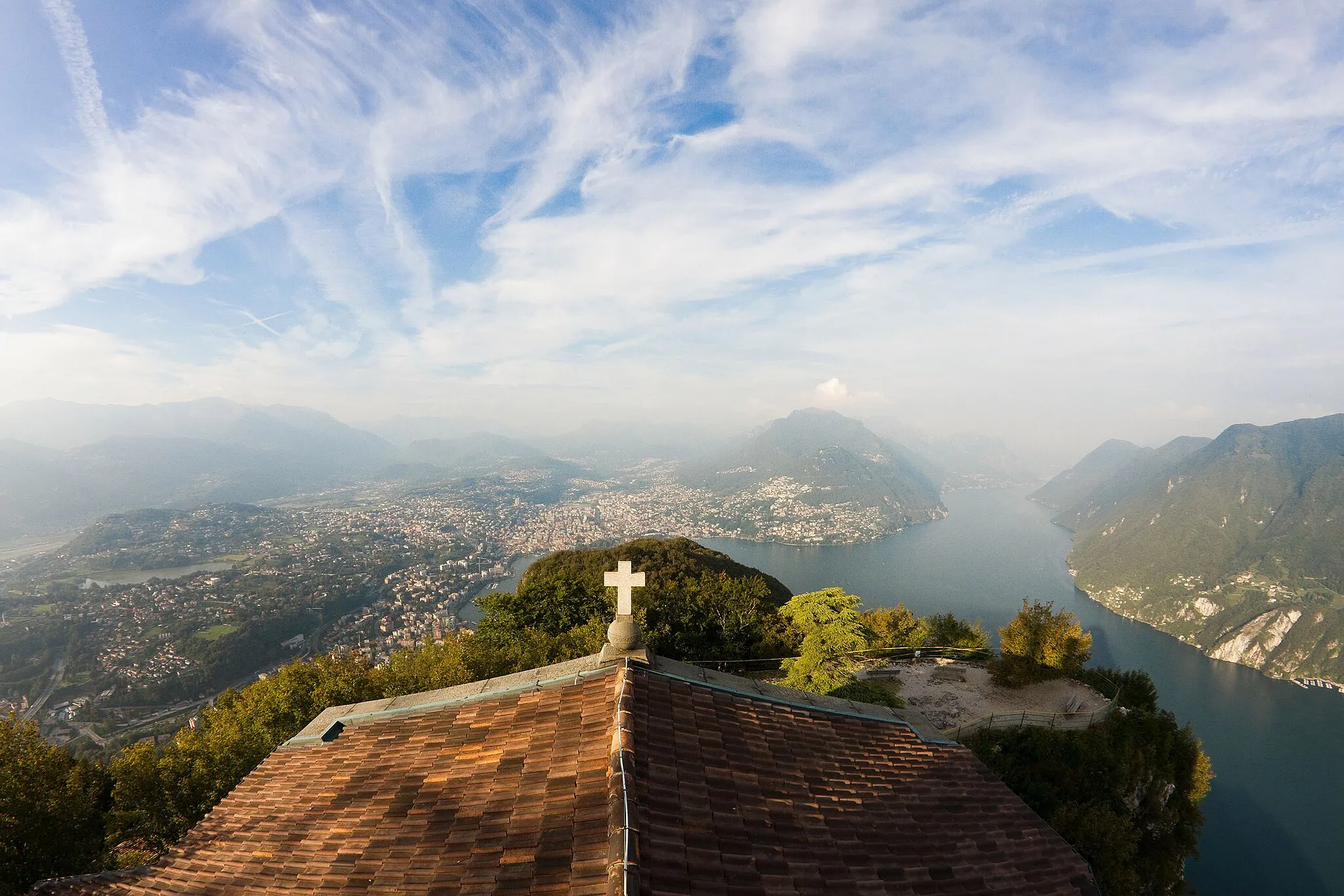 Photo showing: View of the City of Lugano and its surroundings from the top of Monte San Salvatore. On the foreground: the church of San Salvatore, built at the top of the mountain of the same name.