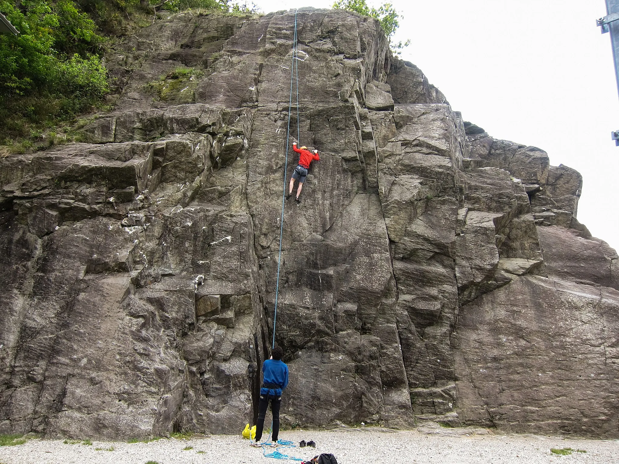 Photo showing: Due arrampicatori praticano arrampicata sportiva alla palestra di roccia  "Il Cinzanino"  della falesia di Maccagno sulla costa del Lago Maggiore in provincia di Varese. L'uomo in blu fa sicura a quello in rosso che scala la parete di roccia salendo "da secondo", cioè con la corda fissata in cima alla parete. La palestra viene gestita dalla sezione CAI di Luino. Foto scattata il 30 aprile 2017.