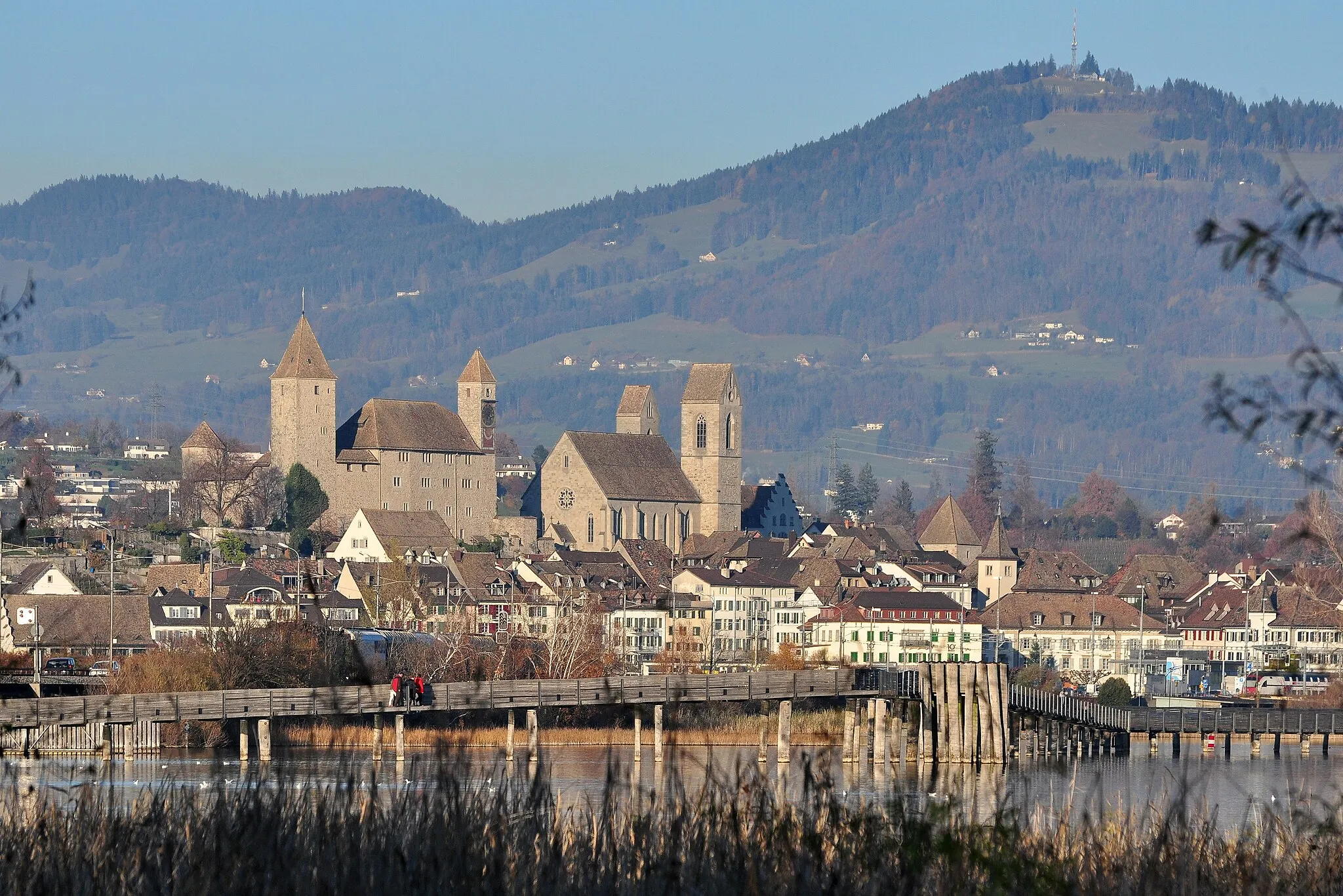 Photo showing: Rapperswil (Switzerland), as seen from Holzbrücke between Rapperswil and Hurden, crossing Obersee (upper Lake Zurich), Seedamm to the left, Bachtel mountain in the background.