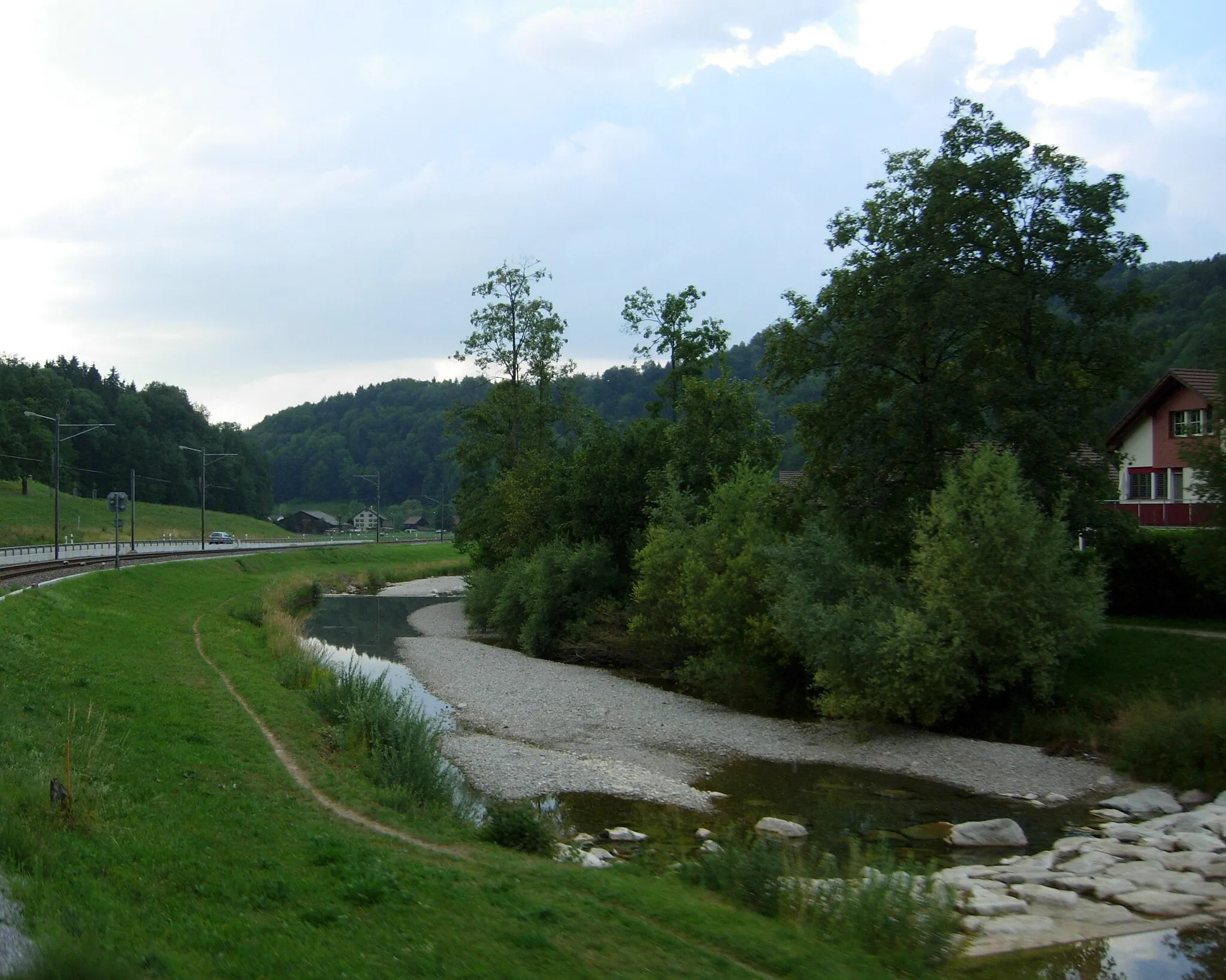 Photo showing: The river Töss is on the right along with some houses. The river is flowing away from the viewer here. A railroad track of the SBB is visible on the left along with a signal. This picture was taken from the S26 train.