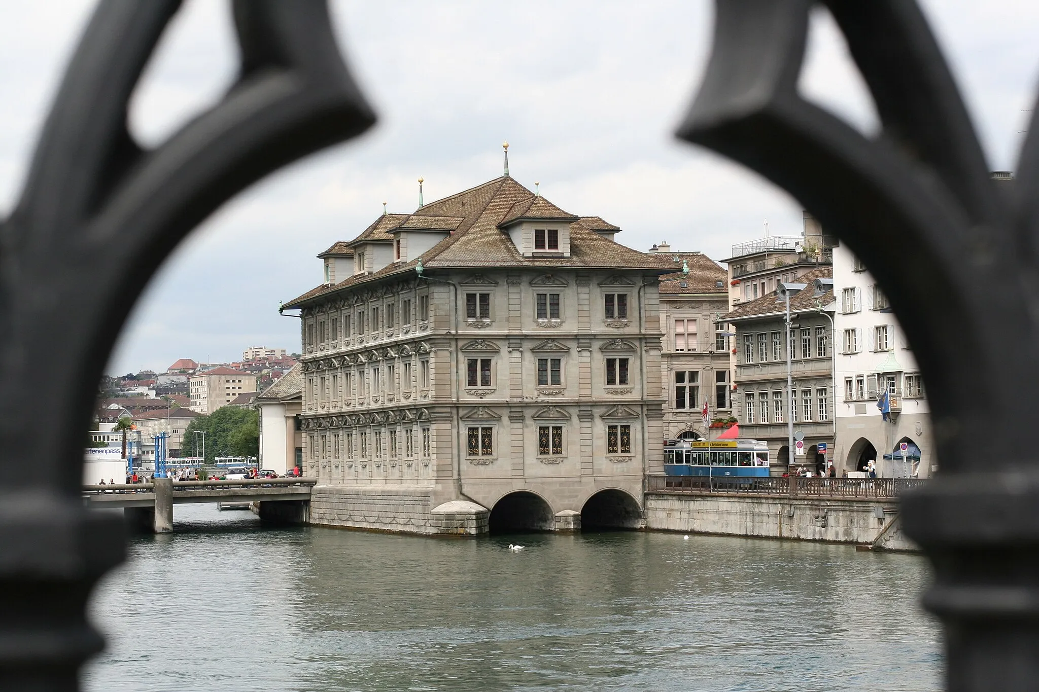 Photo showing: Das Rathaus von Zürich. Es besitzt nur einen Ein- und Ausgang zum Limmatquai hin. Die Fenstergitter im Parterre lassen sich von innen öffnen, damit die Ratsmitglieder im Notfall zur Limmat hin evakuiert werden können. Blick durch das Geländer der Münsterbrücke über die Limmat.