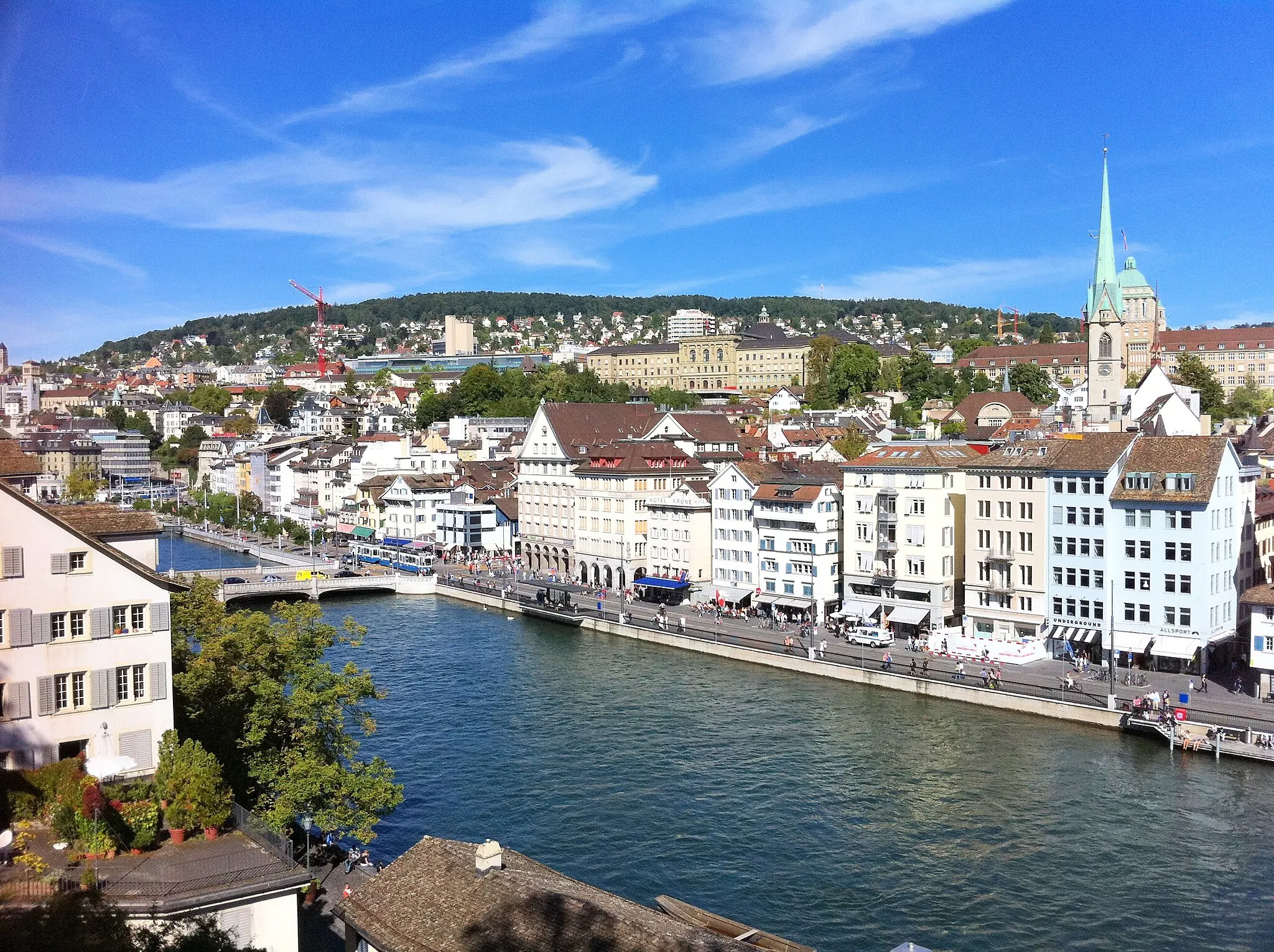 Photo showing: Zurich: View from Lindenhof over River Limmat and the Old Town "Niederdörfli" with the tower of the Predigerkirche. The south side of the hill Zürichberg with University (right) and Federal Technical Highschool.