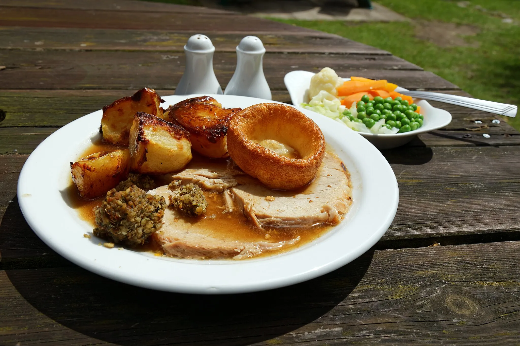 Photo showing: A roast pork Sunday Lunch with roast potatoes, peas, carrots, cauliflower and Yorkshire pudding with stuffing and gravy, in The Crown public house garden at Newgate Street Village (name of road), at Newgate Street, in the civil parish of Hatfield, and the Borough of Welwyn Hatfield, Hertfordshire, England. Camera: Camera: Canon EOS 6D with Canon EF 24-105mm F4L IS USM lens. Software: file lens-corrected and optimized with DxO OpticsPro 10 Elite and Viewpoint 2, and further optimized with Adobe Photoshop CS2.