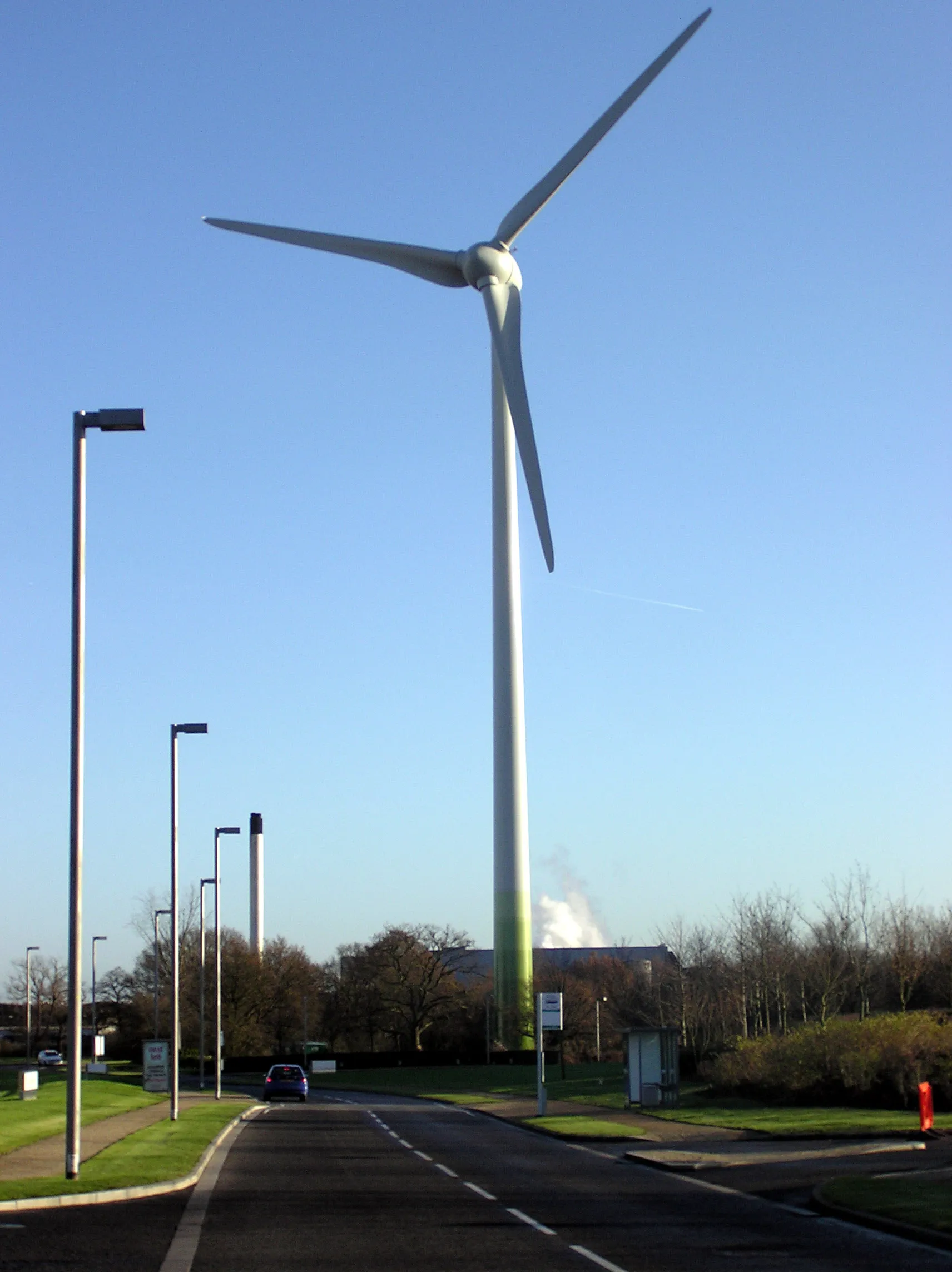 Photo showing: A wind generator at Junction 11 of the M4 motorway, at Greenpark industrial estate, near Reading, Berkshire, England. Construction finished in November 2005. The turbine supplies approx 1000 homes (up to 1,500 local homes and businesses).
The turbine on top of the 85 m (279 ft) tower is the German-made Enercon E-70. The three fibreglass blades are each 33 m (108 ft) long, rotating at 6 to 21 rpm depending on wind speed. Maximum power output of 2.05 MW is reached at a wind speed of 14 m/s (31 mph) then remains constant with increasing wind speed. The hub is kept facing into wind.

At a pre-determined high wind speed the blades cease rotation.