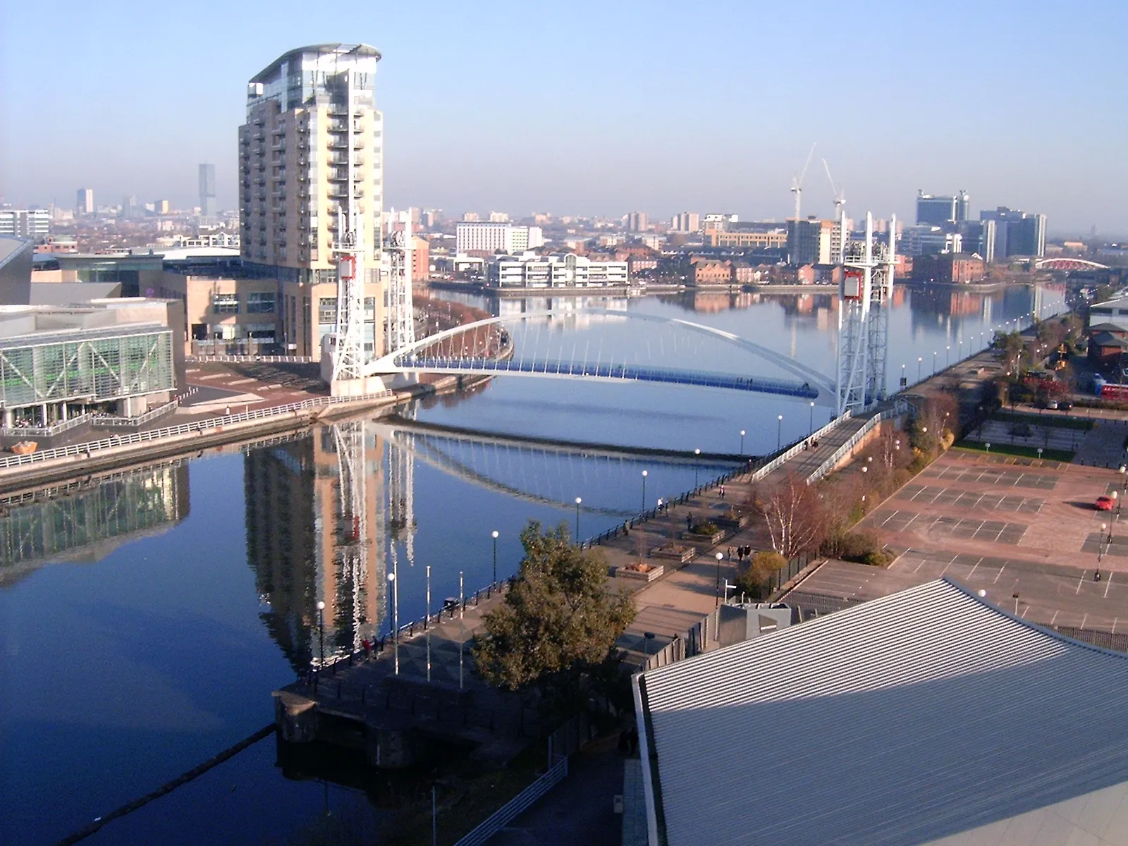 Photo showing: Salford Quays. Left side (north) of Manchester Ship Canal: The Lowry, Lowry Outlet Mall, The Quays. Right side (south): Imperial War Museum North. Millennium Footbridge at centre.