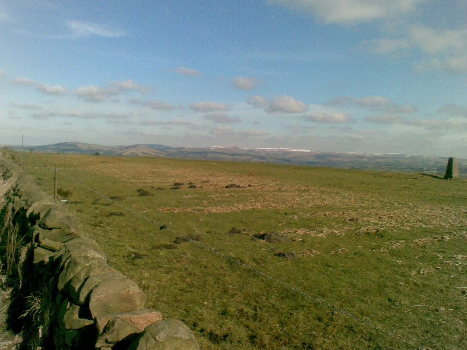 Photo showing: Still snow on the tops From the minor road adjacent to trig point 336 (extreme right of picture) looking towards the Derbyshire Peaks around Buxton where some of the winter snow awaits the warm spring sunshine.  The tower at extreme left of image is the radio mast at Sutton Common, overlooking the A54/A523 road junction and often known locally as "The Totem Pole".