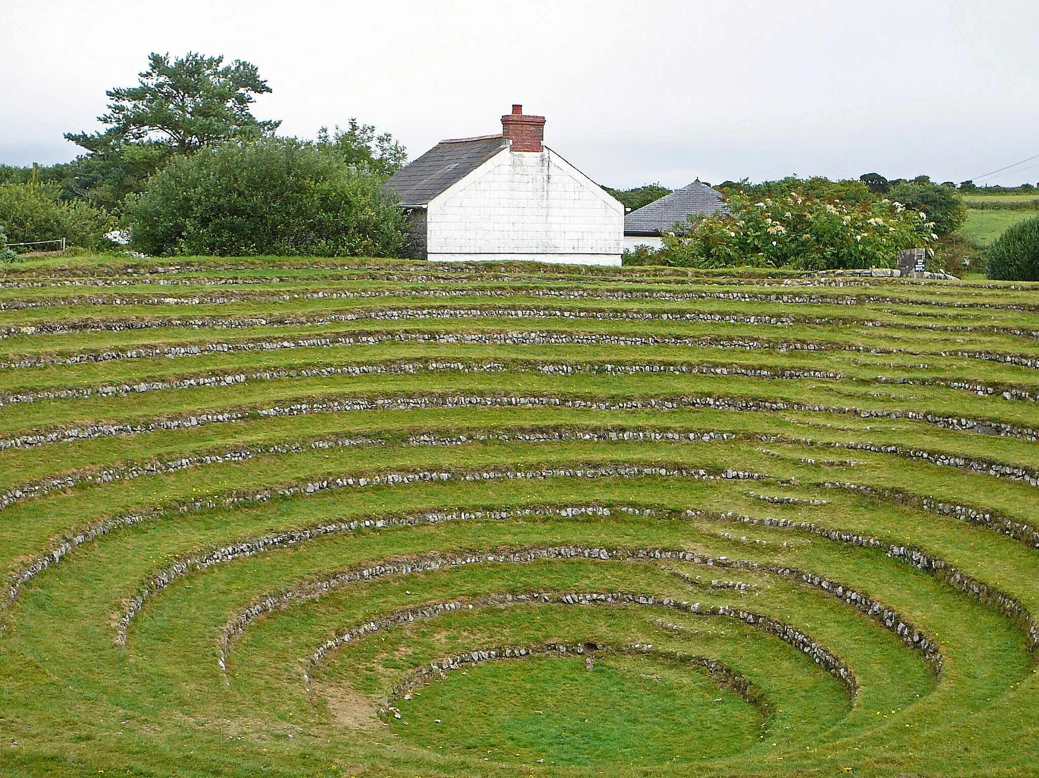 Photo showing: Methodist open air meeting place. 1762, remodelled in 1806. Conical pit made in fallen-in mine shaft which was used by John Wesley for preaching in 1762, and remodelled and reduced in size in 1806, to 360 feet circumference and 16 feet depth, with 13 circles of tufted seating faced with random rubble. On the west side a flight of segmental steps is built into the terraces, and to the north round the 4th step down is a pair of stone posts with a rectangular boulder between them (probably the "pulpit"). Used for Whit Monday services annually from 1807 to 1966.