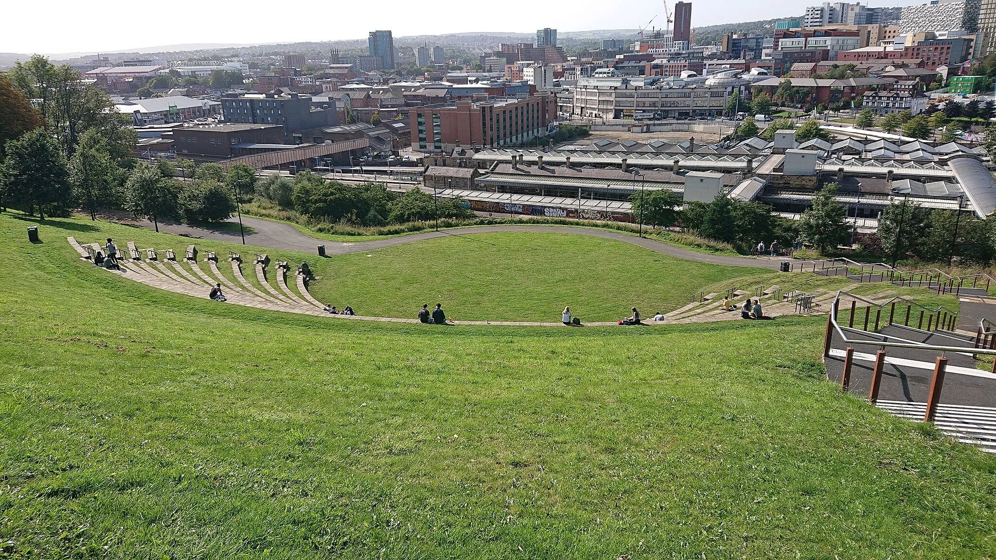 Photo showing: View of the Sheffield Amphitheatre looking down, including the station behind it. Taken from the east. The stairs leading to the station are visible at the near-right edge of the image.