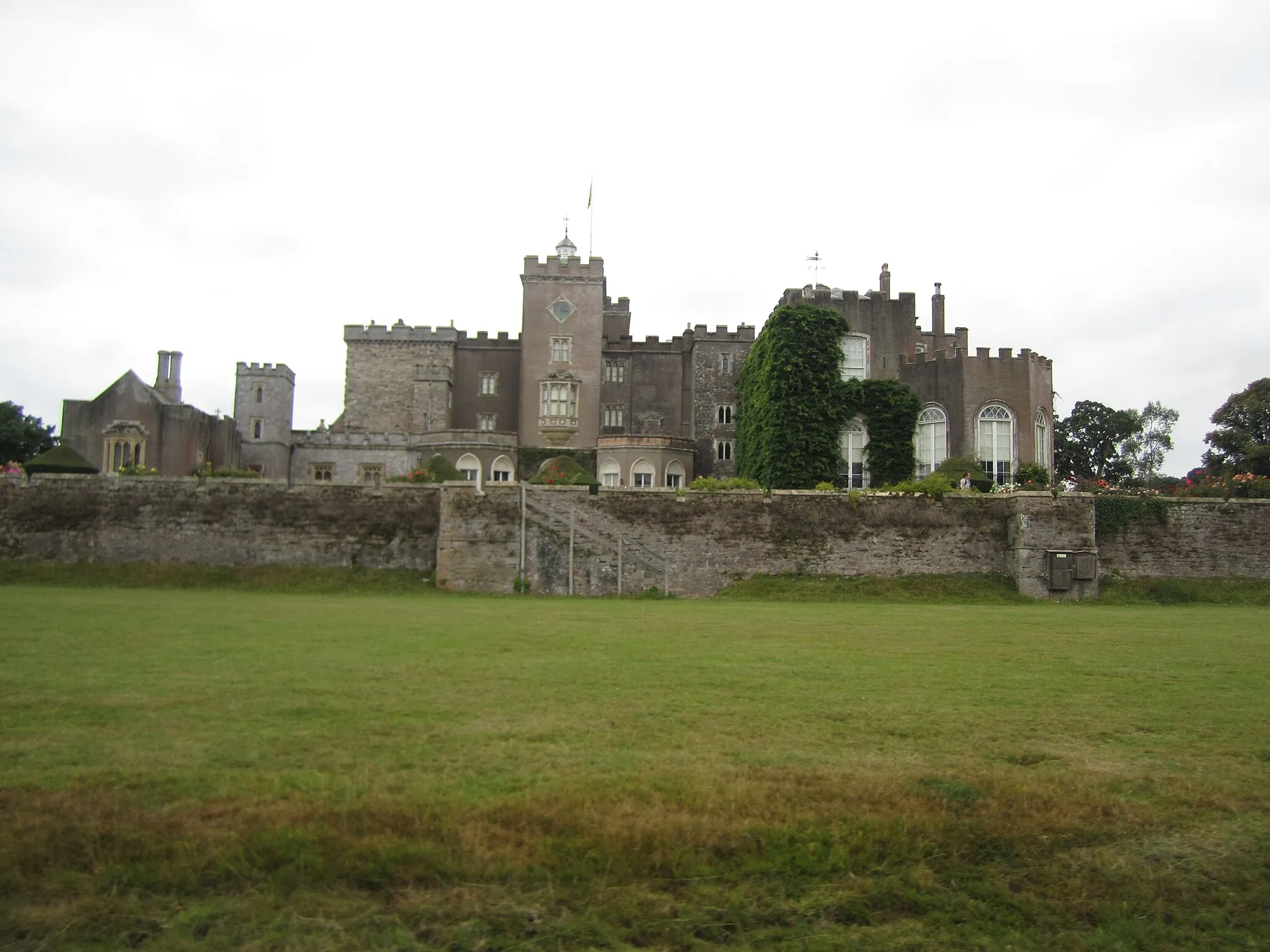 Photo showing: Powderham castle taken from the deer park, showing how it is made of sections of varying age.  The chapel is on the far left and the oldest tower on the middle left