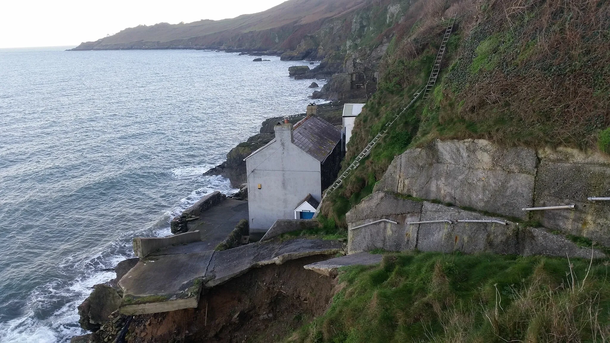 Photo showing: The ruined village of Hallsands in Devon, England. The village was the victim of erosion by the sea and was never rebuilt. Ladders from the clifftop are visible, the main path having fallen away. Start Point and its lighthouse can be seen in the background.