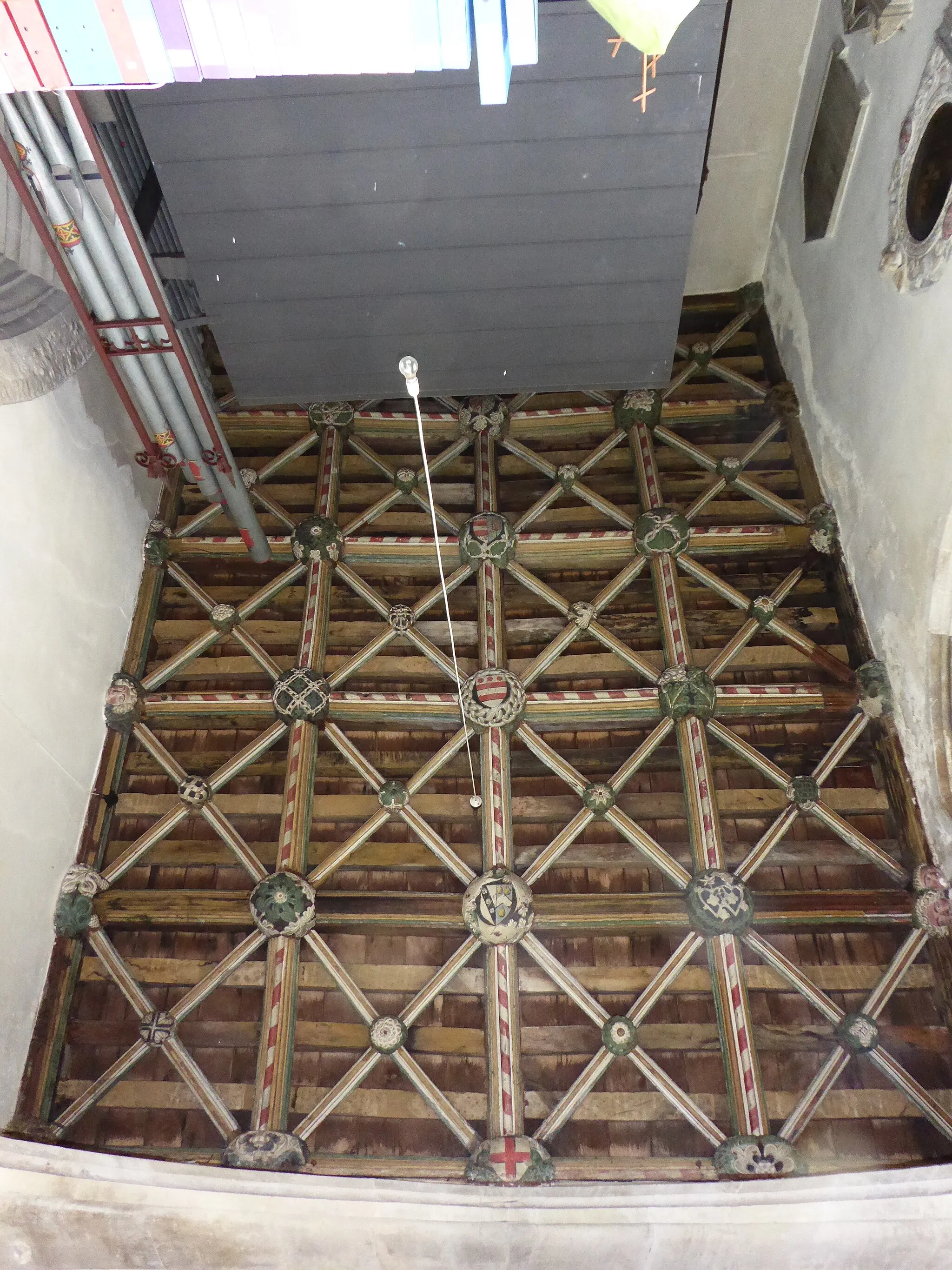 Photo showing: Ceiling of St Bridget's Chapel (North Aisle Chapel / North Chancel Chapel) (early 15th century) within Swimbridge Church, Devon. South at top, north at bottom. John Mules of Ernesborough in the parish of Swimbridge, built this Chapel "the north aisle of the church", according to Risdon, Tristram (d.1640), Survey of Devon, 1811 edition, London, 1811, with 1810 Additions, pp.324. "Repainted in 1727 as a date shows" (Pevsner, Nikolaus & Cherry, Bridget, The Buildings of England: Devon, London, 2004, p.771). For discussion of the heraldry see: Rogers, William Henry Hamilton, The Antient Sepulchral Effigies and Monumental and Memorial Sculpture of Devon, Exeter, 1877, pp.299-301[1] Arms on bosses of central beam, north to south: 1: St George
2: Cary (Argent, on a bend sable three roses of the field) impaling Orchard (Azure, a chevron argent between three pears pendant or). This appears to memorialise the marriage between Sir Philip Cary (died 1437) of Cockington, Devon, and Cristiana de Orchard of (Orchard Wyndham), Somerset (w:Vivian, Lt.Col. J.L., (Ed.) The Visitations of the County of Devon: Comprising the Heralds' Visitations of 1531, 1564 & 1620, Exeter, 1895, p.150)
3: Mules / de Moels of Ernsborough  (Argent, two bars gules in chief three torteaux)
4: Mules impaling Dennis  Dennis of Orleigh in the parish of Buckland Brewer, Devon (Azure, three Danish battle axes erect or). Also shown on the monument in nearby Bishop's Tawton Church to John Mules (d.1633) of Halmpston in the parish of Bishop's Tawton, the inscription on which states his descent from Mules of Ernsborough and from w:John de Moels, 1st Baron Moels (1269–1310) of North Cadbury, Somerset.
5: (obscured by organ) Copleston of Copleston, Colebrooke, Devon (Argent, a chevron engrailed gules between three leopard's faces azure), impaling Azure fretty,  argent (unknown family), overall a bend sinister apparently denoting bastardy (a strip of tape stuck on). Marriage not identifiable from Coppleston pedigree in Vivian, Lt.Col. J.L., (Ed.) The Visitations of the County of Devon: Comprising the Heralds' Visitations of 1531, 1564 & 1620, Exeter, 1895, pp.224-33