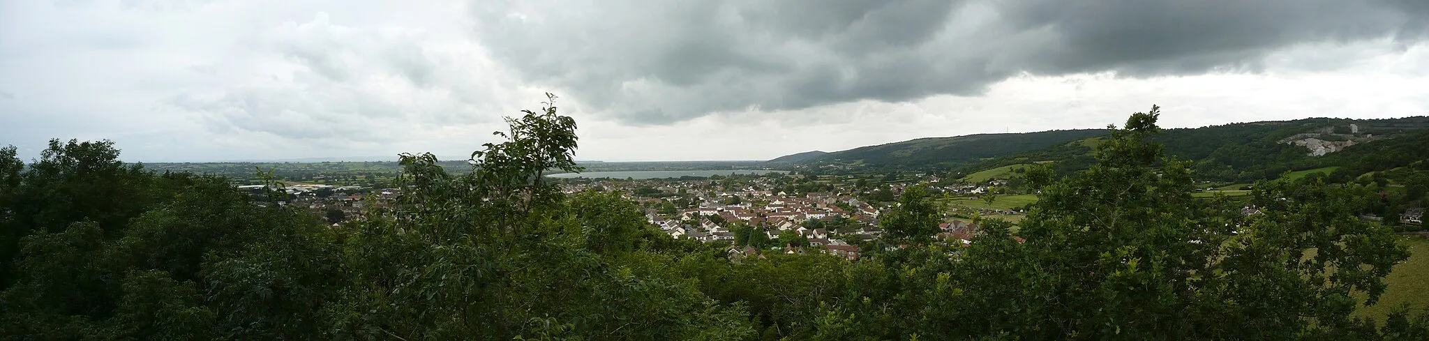 Photo showing: Panoramic view of Cheddar village, Somerset, UK. Cheddar Reservoir seen in the background. Photo taken from Jacob's Ladder on the Mendip Hills.