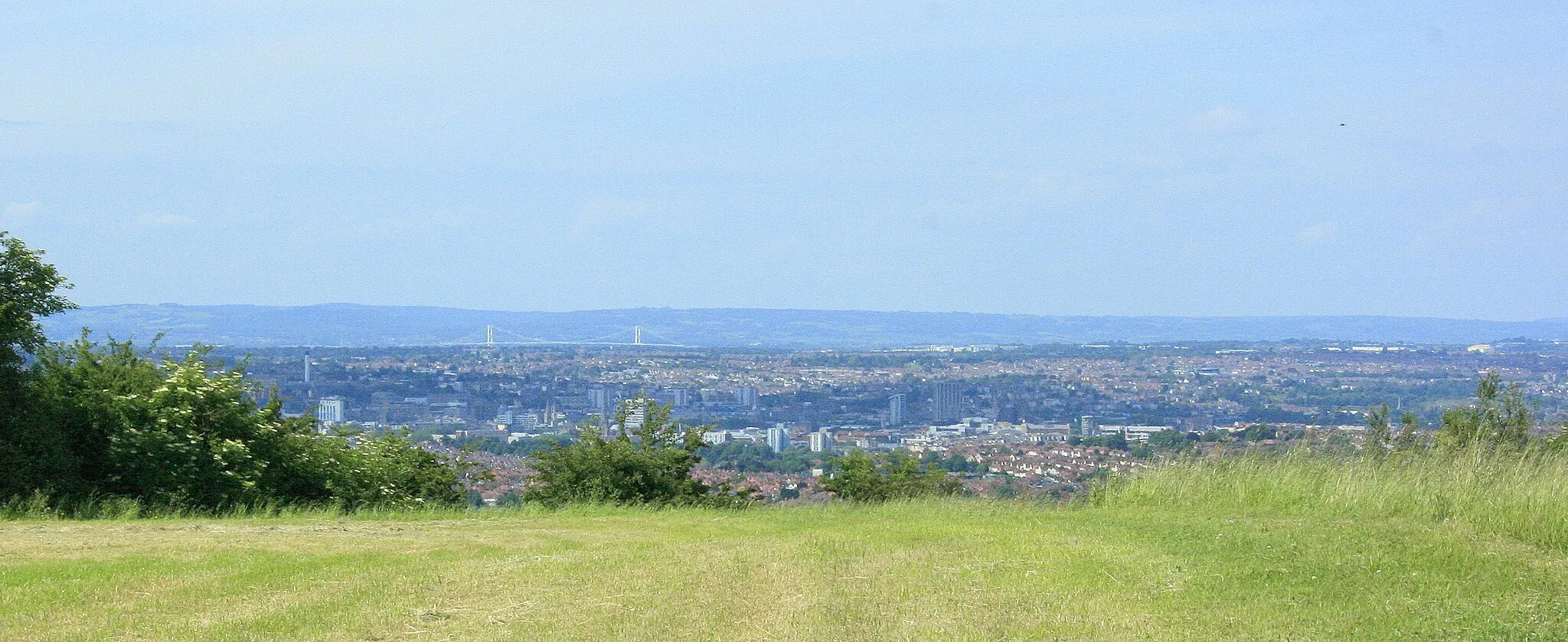 Photo showing: On Maes Knoll "Maes Knoll is an Iron Age hillfort, triangular or rather more Africa-shaped when viewed from the air, ....... It occupies the Oolite ridge that commands the hills south of Bristol. This ridge, which stretches from Dundry Hill to Maes Knoll, steeply descends down to the north and the Avon Valley, creating a fine view over the Lower Avon Valley from Clifton Gorge to the Cotswold escarpment."
The above was copied from: http://www.wansdyke21.org.uk/wansdyke/wanwesteast/wanwest1.htm

--------------------------

The two white towers in the distance are about all that can be seen in this image of the Severn Suspension Bridge between Aust and Beachley. ST5590