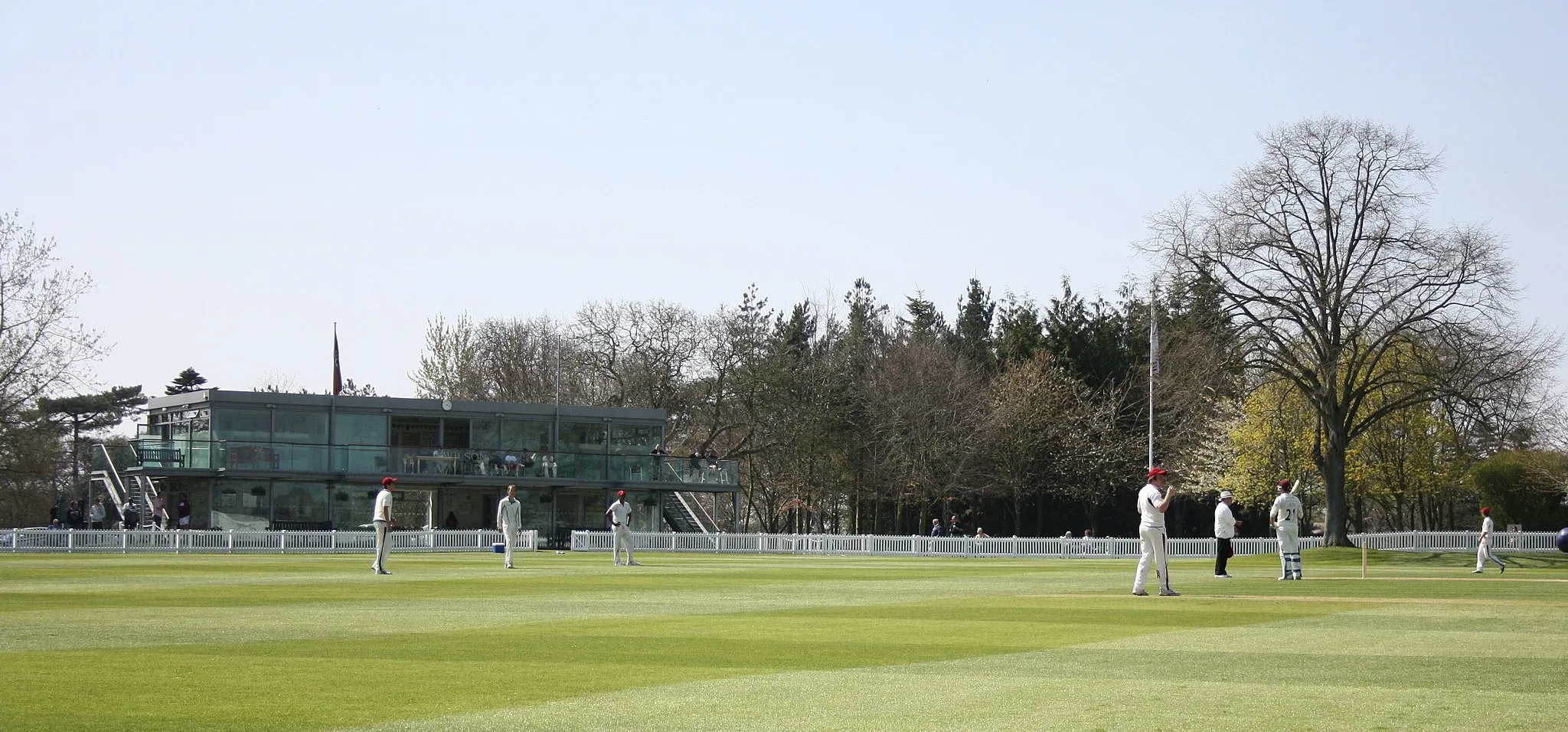 Photo showing: Main cricket ground at Millfield School, showing the pavilion.  Note the tree on the right hand side of the image, which is within the boundary.  The match is being played between a Millfield XI and Somerset County Cricket Club's Second XI.