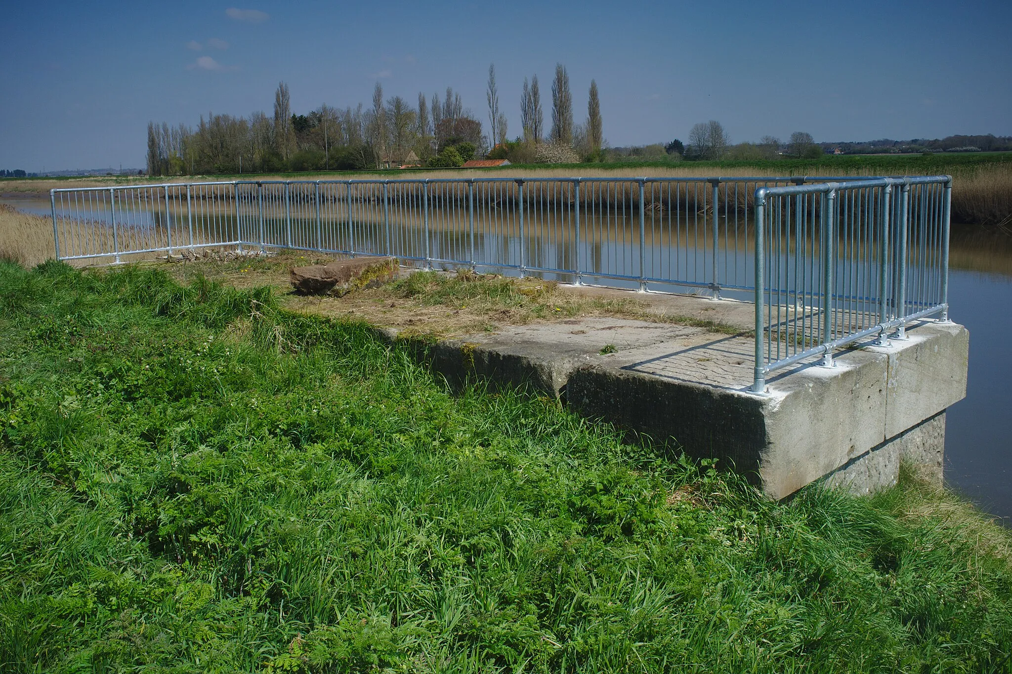 Photo showing: A bridge abutment, with railings (which were added in probably early 2021, see File:River Ouse, Railway bridge abutment, Magdalen.jpg for ones without) in Magdalen, Norfolk. This was for a bridge that used to carry the Wisbech line over the River Great Ouse.