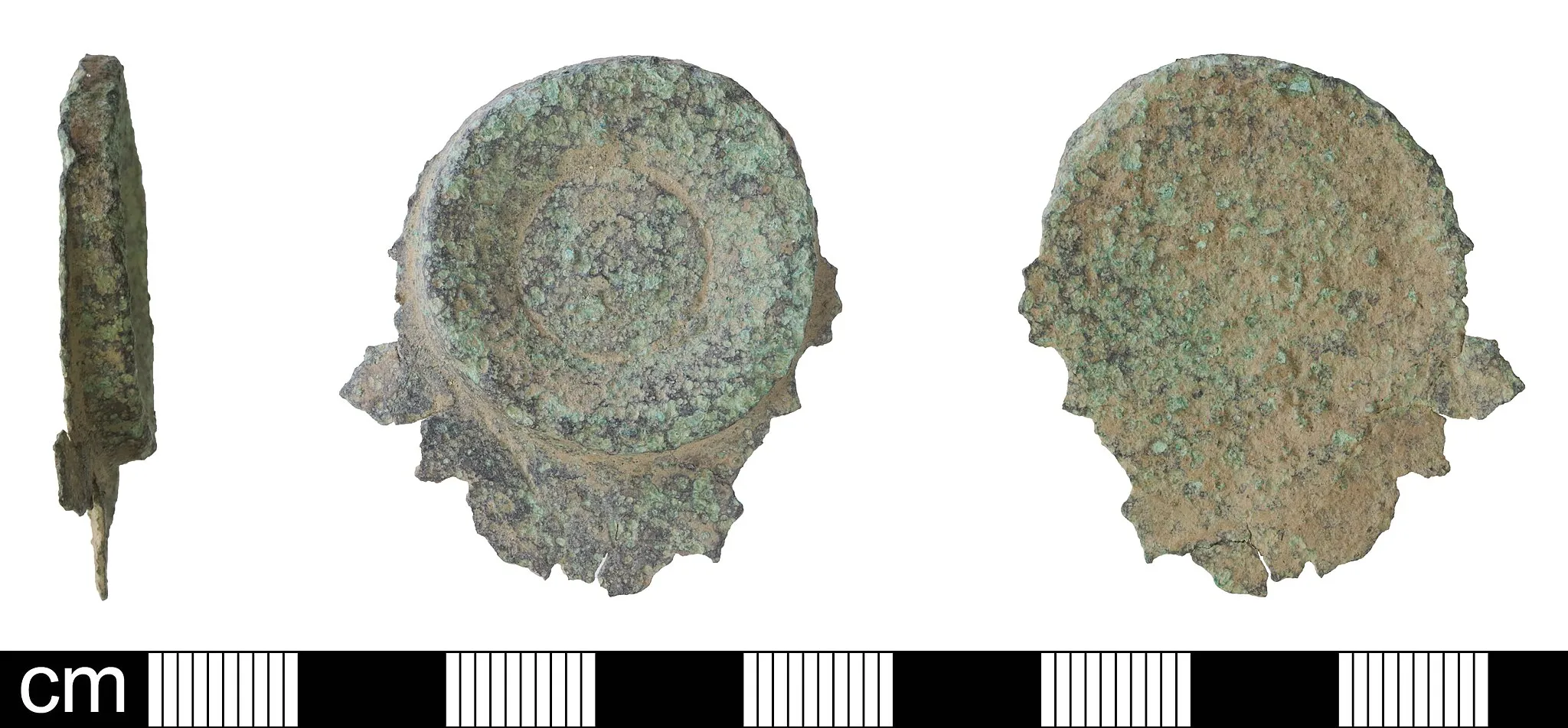 Photo showing: Corroded fragment of Roman copper alloy vessel, probably a bowl, comprising part of the base with foot-ring. Basal diameter 27mm. Vessel wall 1mm thick, basal ring 4mm thick. Weighs 12.89g. Perhaps 2nd or 3rd century.