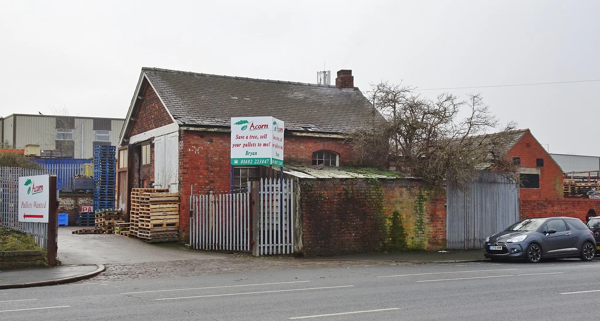 Photo showing: Hedon Road, Kingston upon Hull Victoria Dock Station, Hedon Road. Withernsea line trains were rerouted to run into Hull Paragon Station from 1 June 1864; Victoria Dock Station was henceforth closed to passenger trains. Much of the site was cleared for the construction of Garrison Road in the 1970s. Today, the remaining site is occupied by South Orbital Trading Park. The only remaining feature from the original station site is part of the brick-built boundary wall. Beyond the wall is a former North Eastern Railway (NER) building, today used by Acorn Pallets, No.130 Hedon Road.