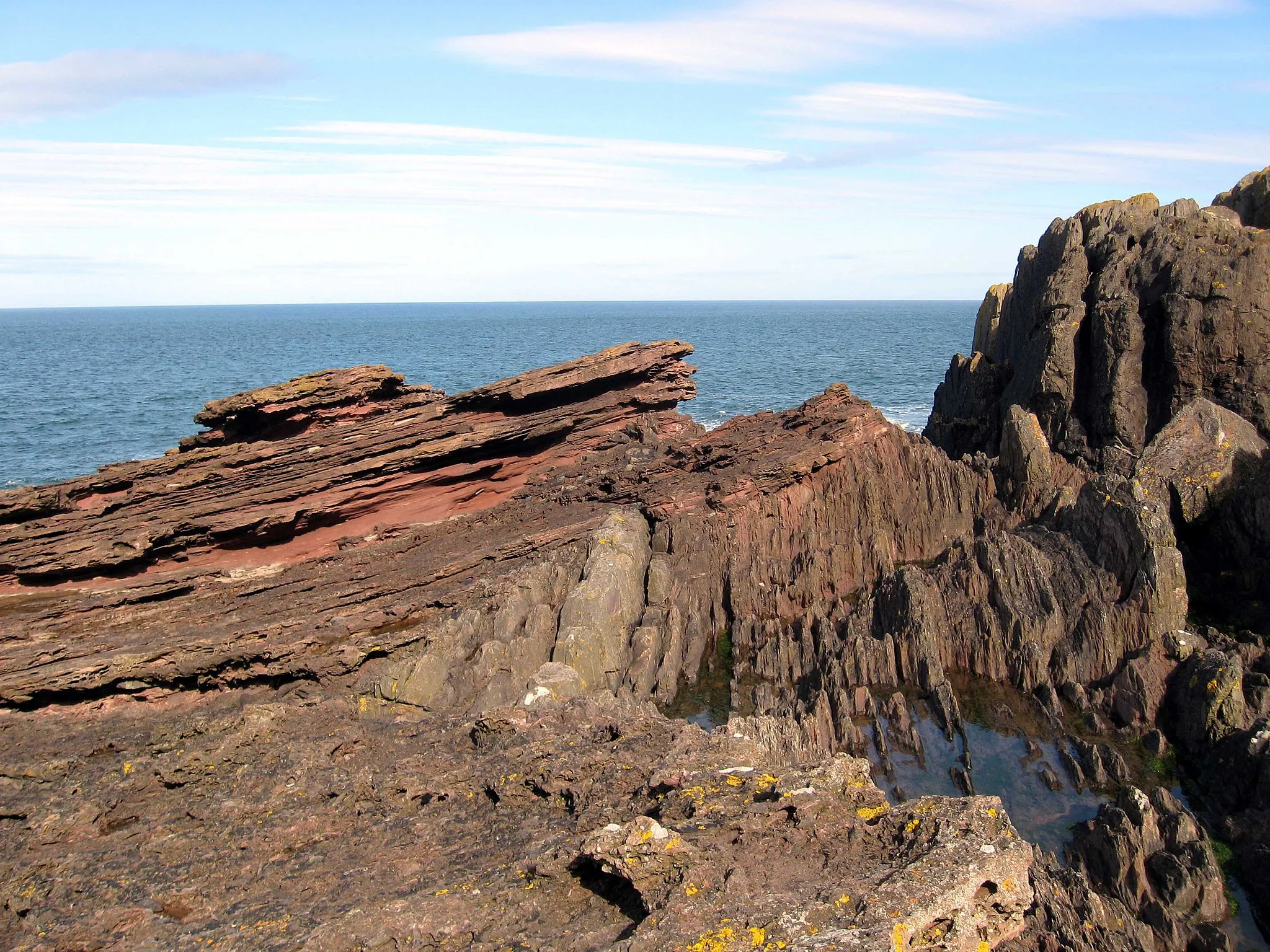 Photo showing: Siccar Point, eroded gently sloping Devonian Old Red Sandstone layers forming capping over conglomerate layer and older vertically bedded Silurian greywacke rocks.
