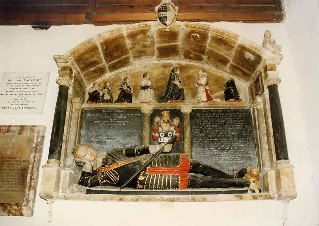 Photo showing: St Giles, Great Maplestead, Essex - mural monument in the Deane Chapel (south chapel) to Sir John Deane (1583-1626), of Dyne's Hall, Great Maplestead, MP for Essex in 1625 and High Sheriff of Essex for 1610–11, Deputy Lieutenant and JP for Essex, 1625. A magnificent monument to his wife survives in the same church. His semi-recumbent effigy wears full armour.[1]
Inscription
Left tablet[2]:
Memoriae Sacrum Johannis Deane Equitis Aurati Equitatus in Agro Essexiensi Propraefecti quem moribus suavissimis integerrimisq(ue) annum aetatis 43 agenti D O M  ….Ipsius …. popular … militum sed  maxime anni …. uxoris prolisq(ue) numerosi nobis ademit. Anna uxor maestissima cum publico bonoru(m) juncta privatoq(ue) totius stemmatis morori posuit AD 1628 ("Sacred to the memory of John Deane, Knight Bachelor, Deputy Lieutenant in the County of Essex ...... Anne his most grieving wife ... placed (this monument) in 1628") Right tablet (see legible image[3]):
Lett Posterity know Sr John Deane of Dines Hall in Great Maplestead in ye County of Essex Knt, one of ye Deputy Lieutenants & Justices of Peace in ye same Shyre who was descended from ye worthy family of ye Deanes of Lancashire & who match’t with Mrs (Mistress) Anne Drury of ye honourable tribe of ye Druries of Riddleworth in Norfolk by whom hee had 6 daughters and 2 sonnes (1: Katharine 2: Dru 3: Anne 4: Elizabeth 5: John 6: Dorcas 7: Frances 8: Mildred) dyed on ye 17th day of February in ye yeare of his life 43 & in ye yeare of Grace 1625. His parts & person were admirable. Desarte & hee were twynns. His pietye was ye fountaine of his actions & his hearte was ye seate of equitye. Truth was ye best interpretour of his words. His meditations were wholy bounded in Heaven. His charitye asked tyme to give & gave no tyme to asking. Ye pleasures of his life were ye passages of virtue. Death was his triumphe not his conquerour. He was buried in ye teares of ye faithfull & shall rise in ye joy of ye Righteous. To whose perpetuall memory Anne Deane his eldest daughter did make & dedicate this inscription. Heraldry
Sable, a fess ermine between three chaplets argent (Deane of Dyne's Hall, Great Maplestead, Essex) (Burke, Sir Bernard, The General Armory, London, 1884, p.271 "Deane of Maplestede, Essex and Blackburne, Lincolnshire; Deane of Gosfield, Essex (Granted 1577, per Grantees of Arms ed. W.H. Rylands (Harl. Soc. lxvi), 72., quoted in History of Parliament biography of Sir John Deane (1583-1626), of Dyne's Hall, Great Maplestead, MP for Essex in 1625[4])) impaling: Argent, on a chief vert a cross tau between two mullets pierced or (Drury), damaged. The same arms appear on the monument to his wife Anne Drury, but show the arms of Drury with chief gules, should be vert. Crest of Deane on helm above shield and as footrest: A bear's head or muzzled gules.

Text per stepneyrobarts.blogspot.com[5]:

On the east wall is Sir John Deane, Deputy Lieutenant and JP for Essex, 1625, of alabaster and marble, set in a recess, with Ionic side columns and a reclining effigy in plate armour with his feet on a muzzled Bear's head. A shelf at the back shows the kneeling figures of his widow, four daughters and two sons and the monument includes two coats of arms. Opposite him on the west wall is a monument to Anne Drury, his wife, dated 1633, erected by her son, Sir Drew Drury, of alabaster and marble with a projecting shelf resting on Ionic columns supporting the recumbent figure, in plate armour of Sir Drew. A large round headed recess at the back contains the upright figure of Lady Anne in a shroud with a broken pediment at the top with two angels and flanked by two arm cartouches. Her epitaph is no less fulsome: Her shape was rare: Her beauty exquisite
Her wytt accurate: Her judgement singular
Her entertainment harty: Her conversation lovely
Her harte merciful: Her hand helpful
Her courses modest: Her discourses wise
Her charity Heavenly: Her amity constant
Her practise holy: Her religion pure
Her vowes lawful: Her meditations divine
Her faith unfaygned: Her hope stable
Her prayers devout: Her devotions diurnall

Her dayes short: Her life everlasting